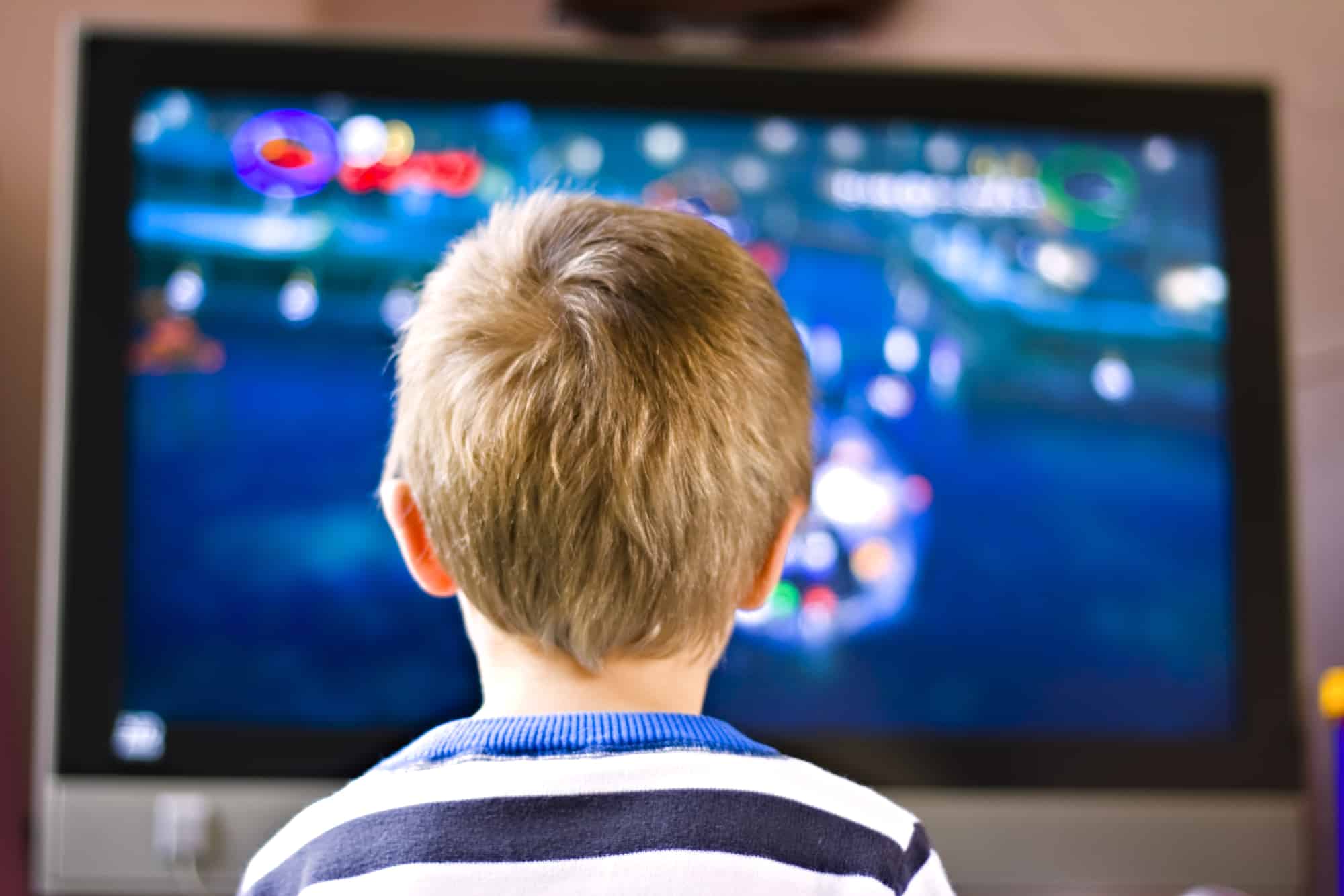 The back of a little boys head in front of an active TV screen.