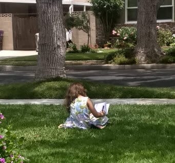 Young girl sitting in her front yard writing in a Notebook.