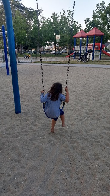 Little girl on a swing set at a park in a play area.