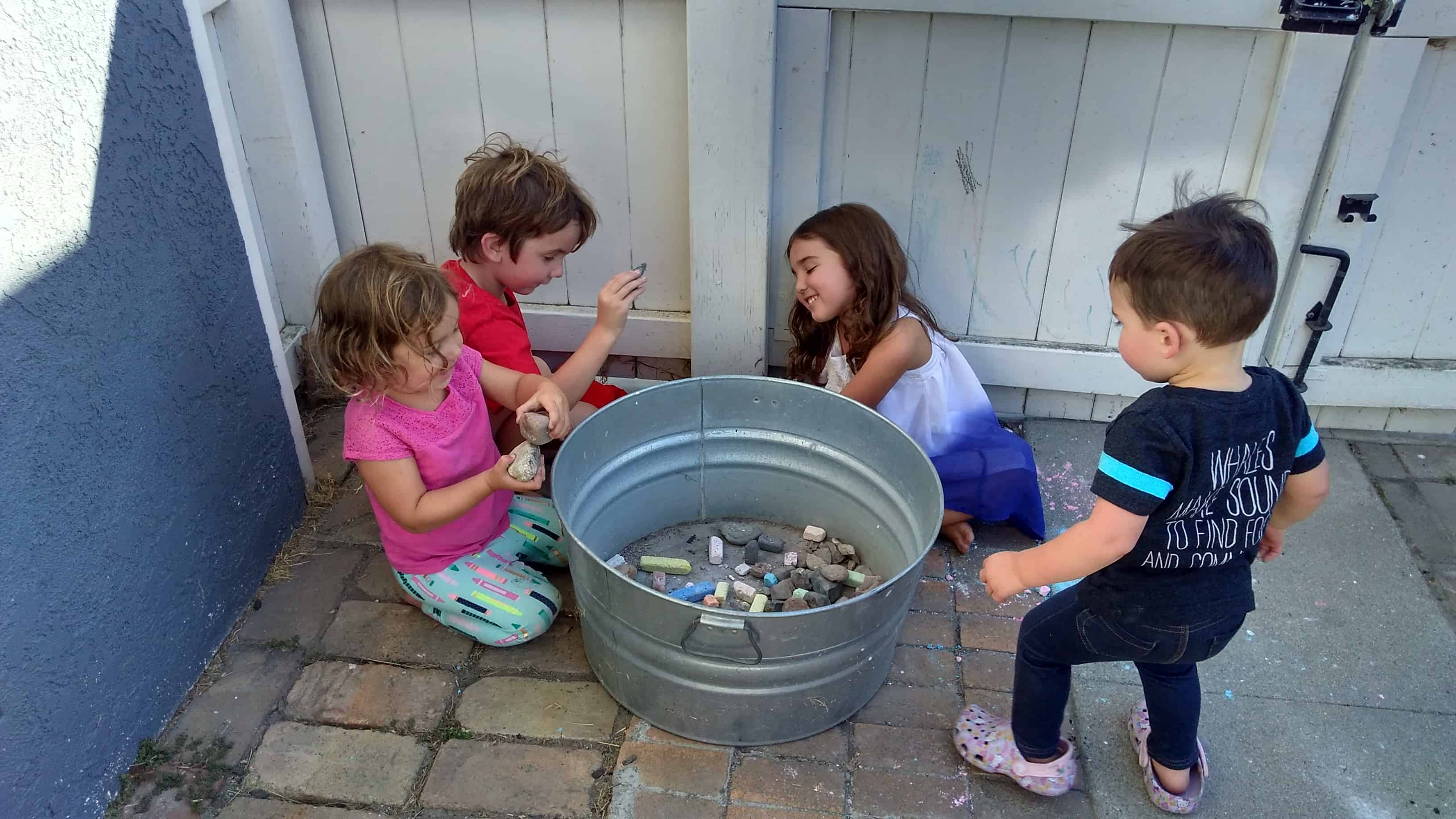 Four children placing rocks in a tin barrel