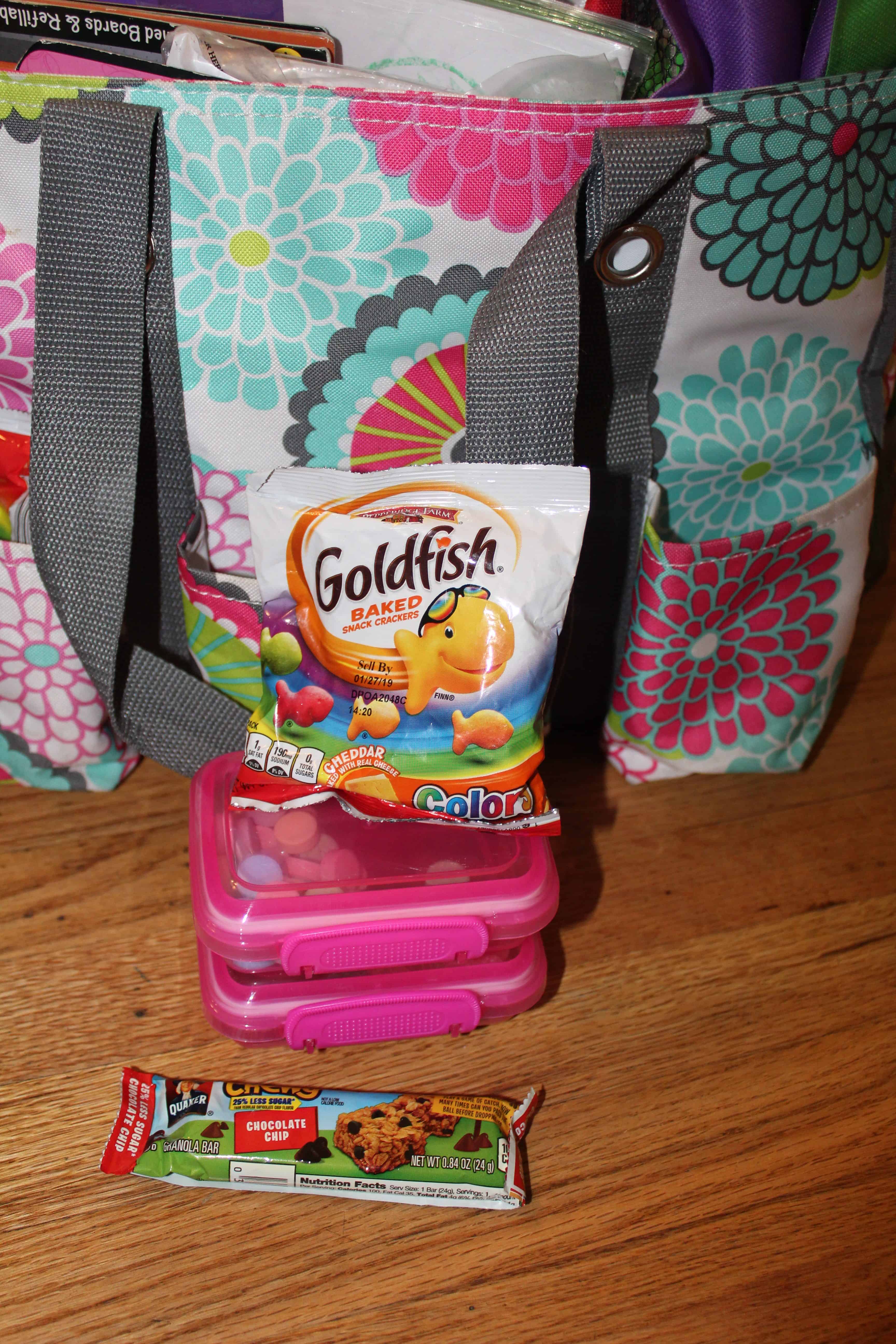 A bag of gold fish, a chewy granola bar and containers of non perishable snacks for the travel activity bag. 