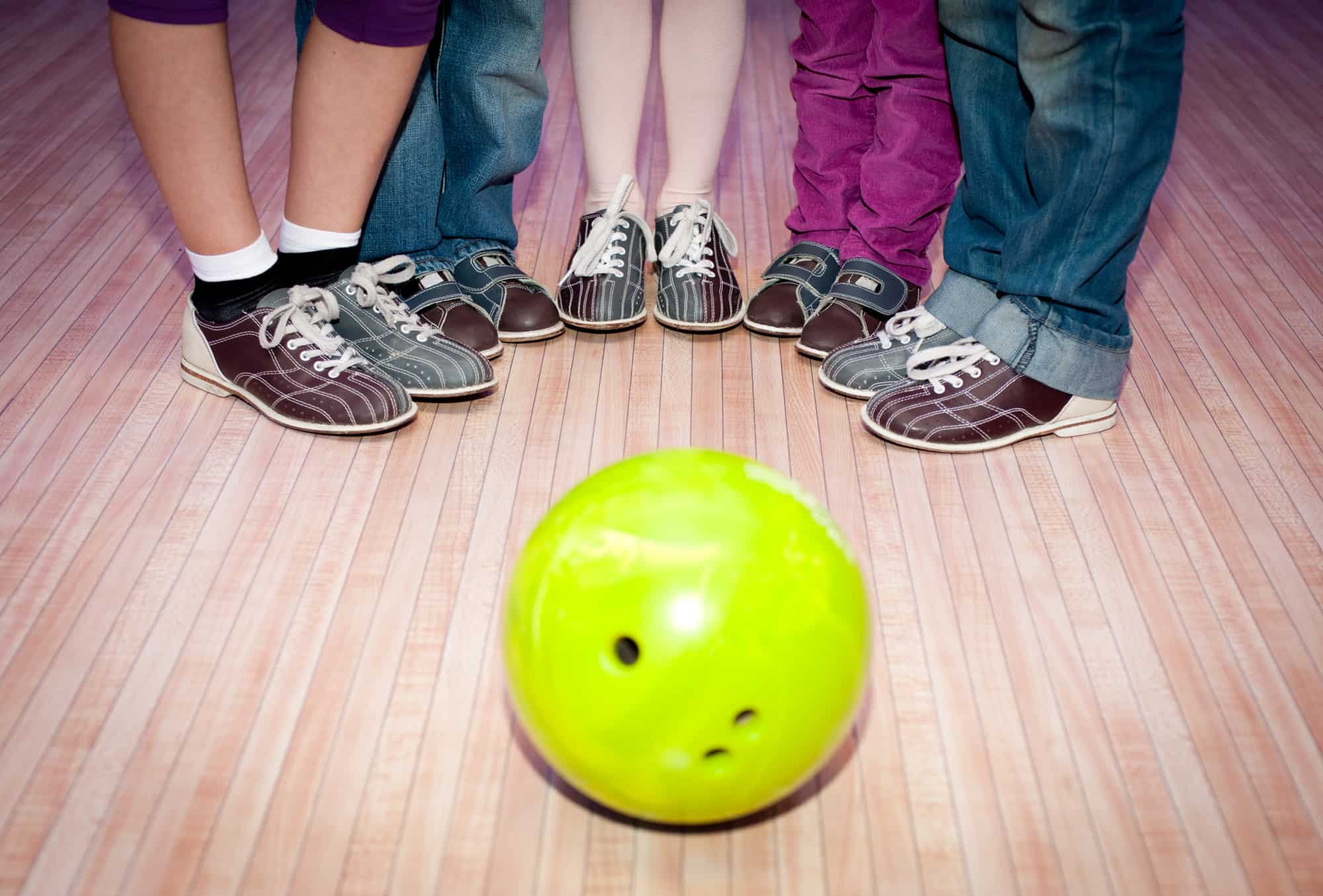 Five different sets of feet representing a family standing around a bowling ball.