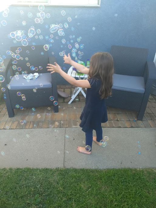 Child extending arms and playing with blown bubbles. 