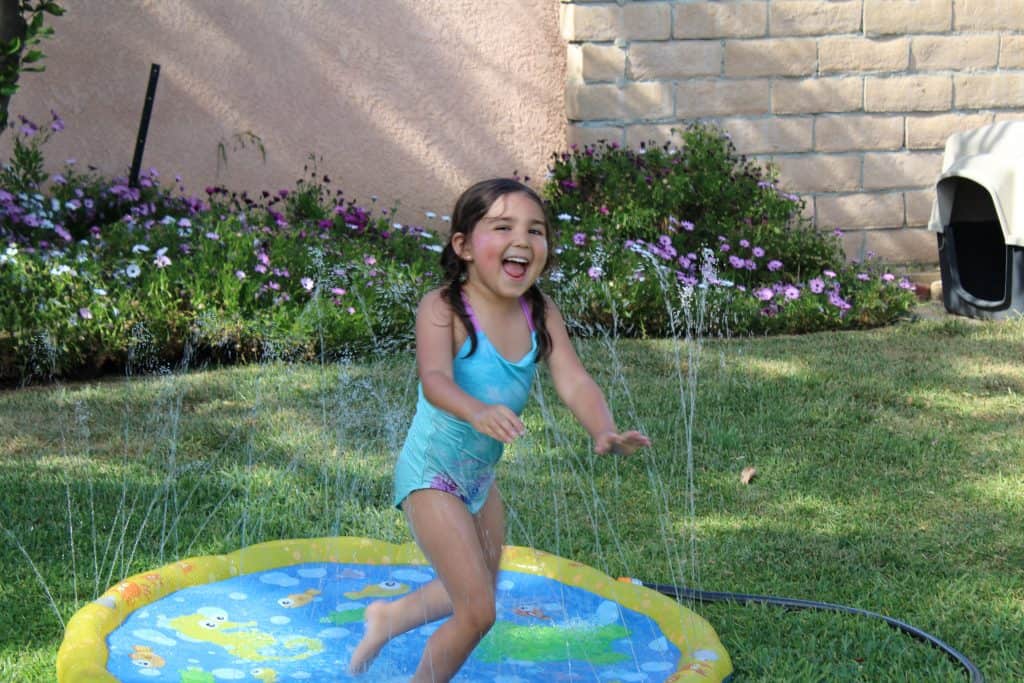 little girl jumping in a sprinkler splash pad