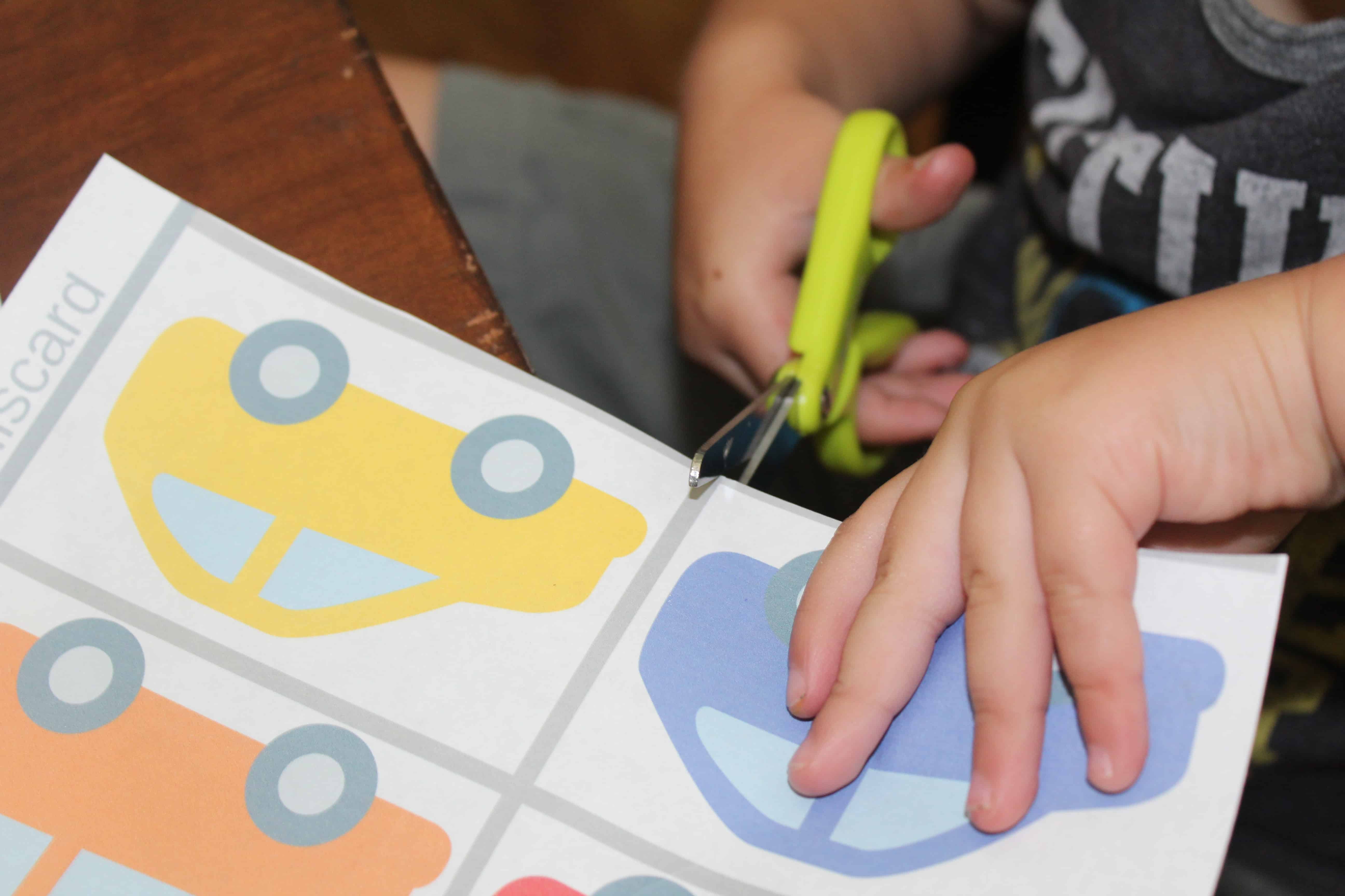 Toddler with safety scissors cutting out car printouts from the activity pack. 