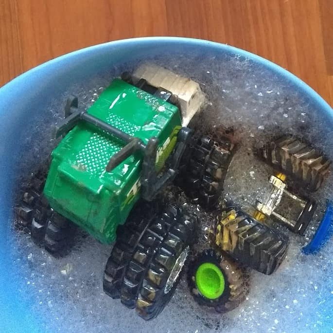Two toy trucks in a bowl full of warm soapy water 