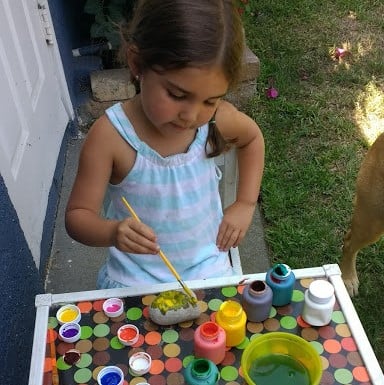 Child using a paint brush and paints to paint a rock. 