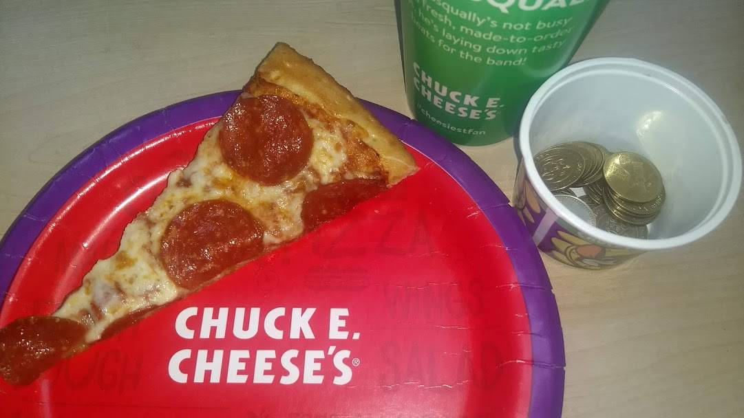 A plate of pizza and a cup of tokens from Chuck E cheese weekday buffet.