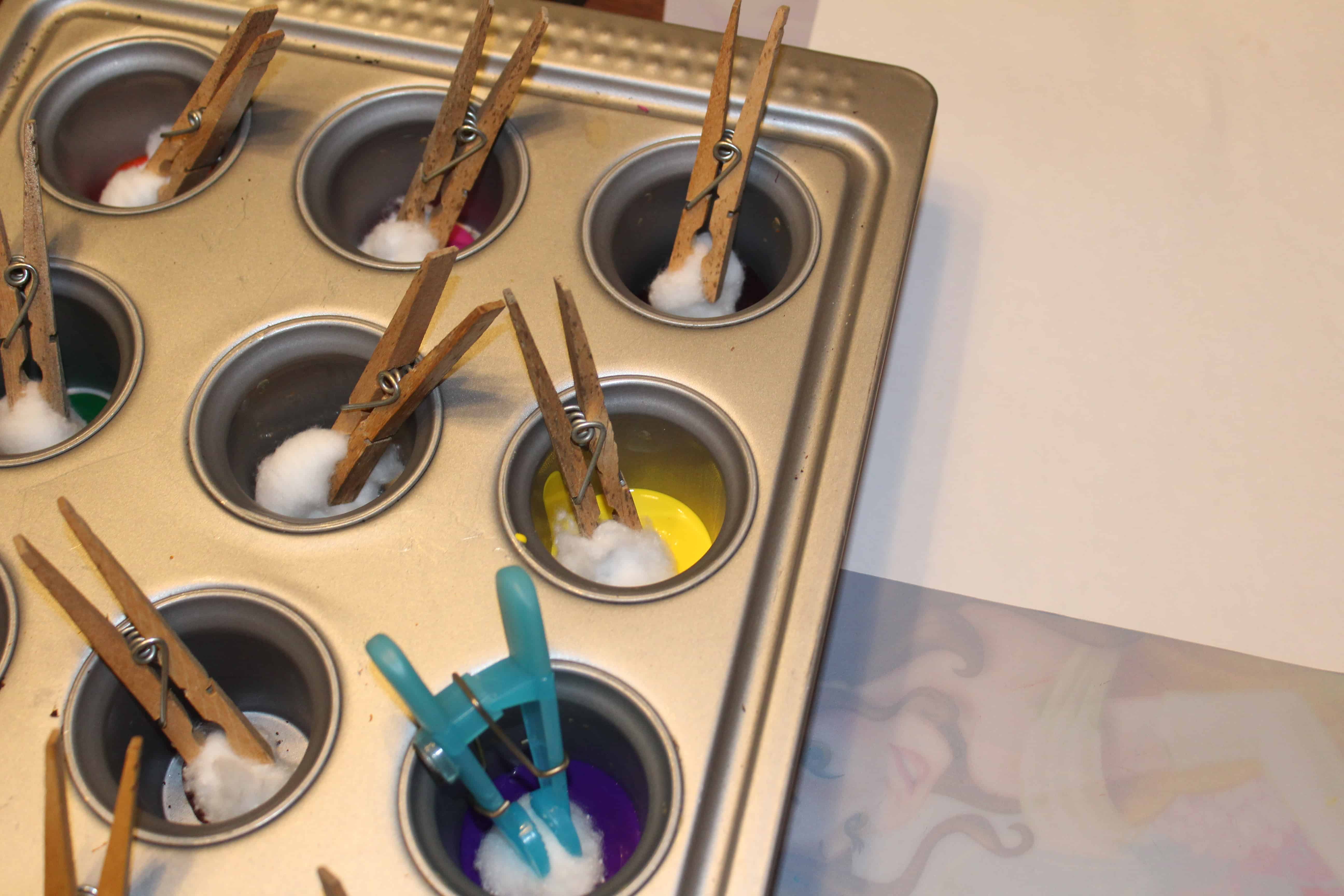 Cupcake tin with different paints in each compartment. Cotton balls held by clothespin dipped in. 