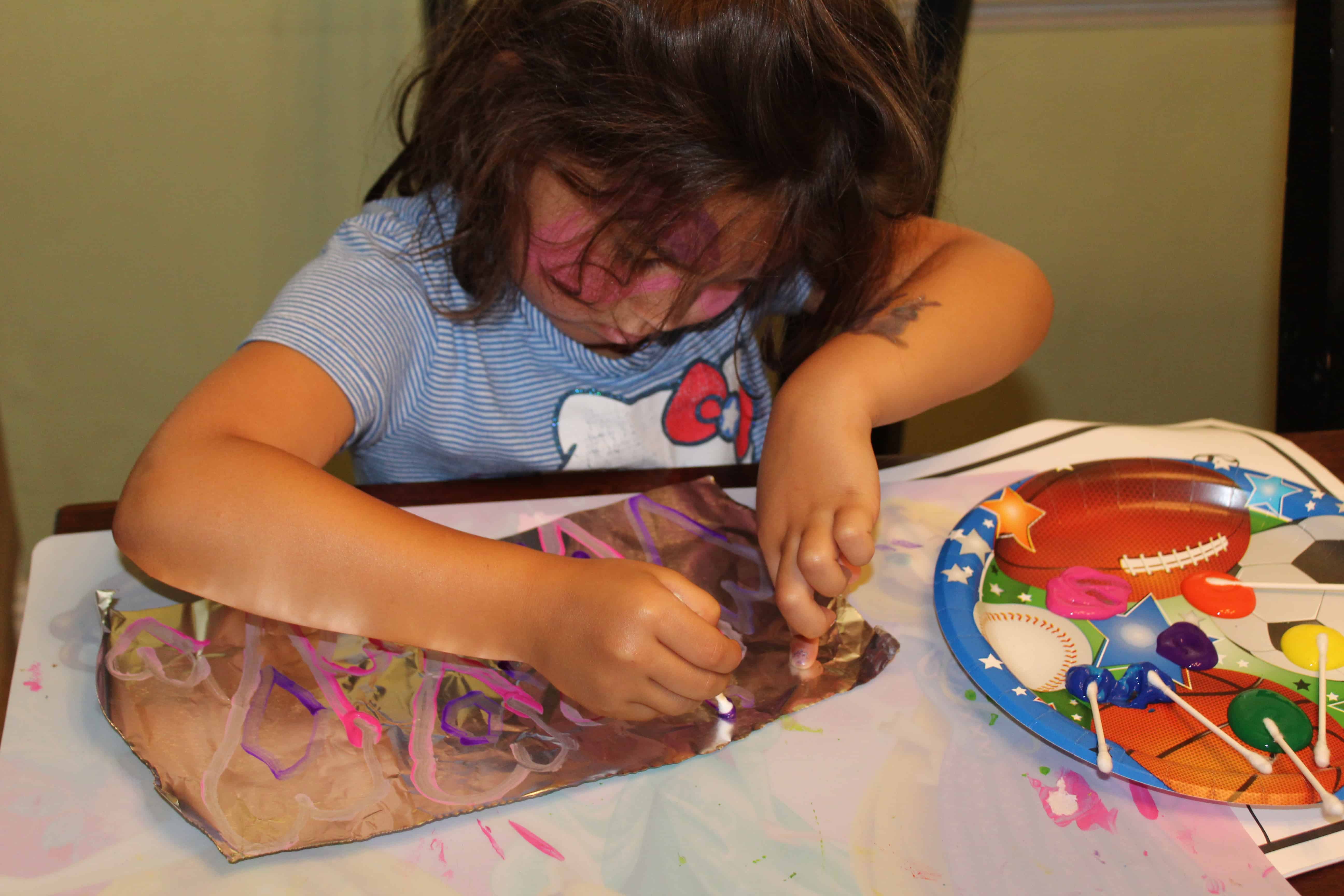 A child painting a sheet of foil with paints using cotton swabs.