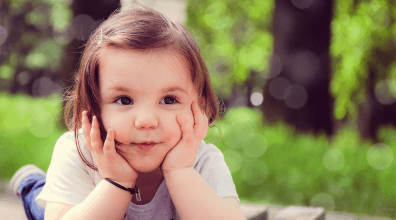 Toddler with a smirk on face resting her chin on her hands. 