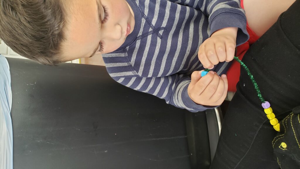 child putting beads on a pipe cleaner