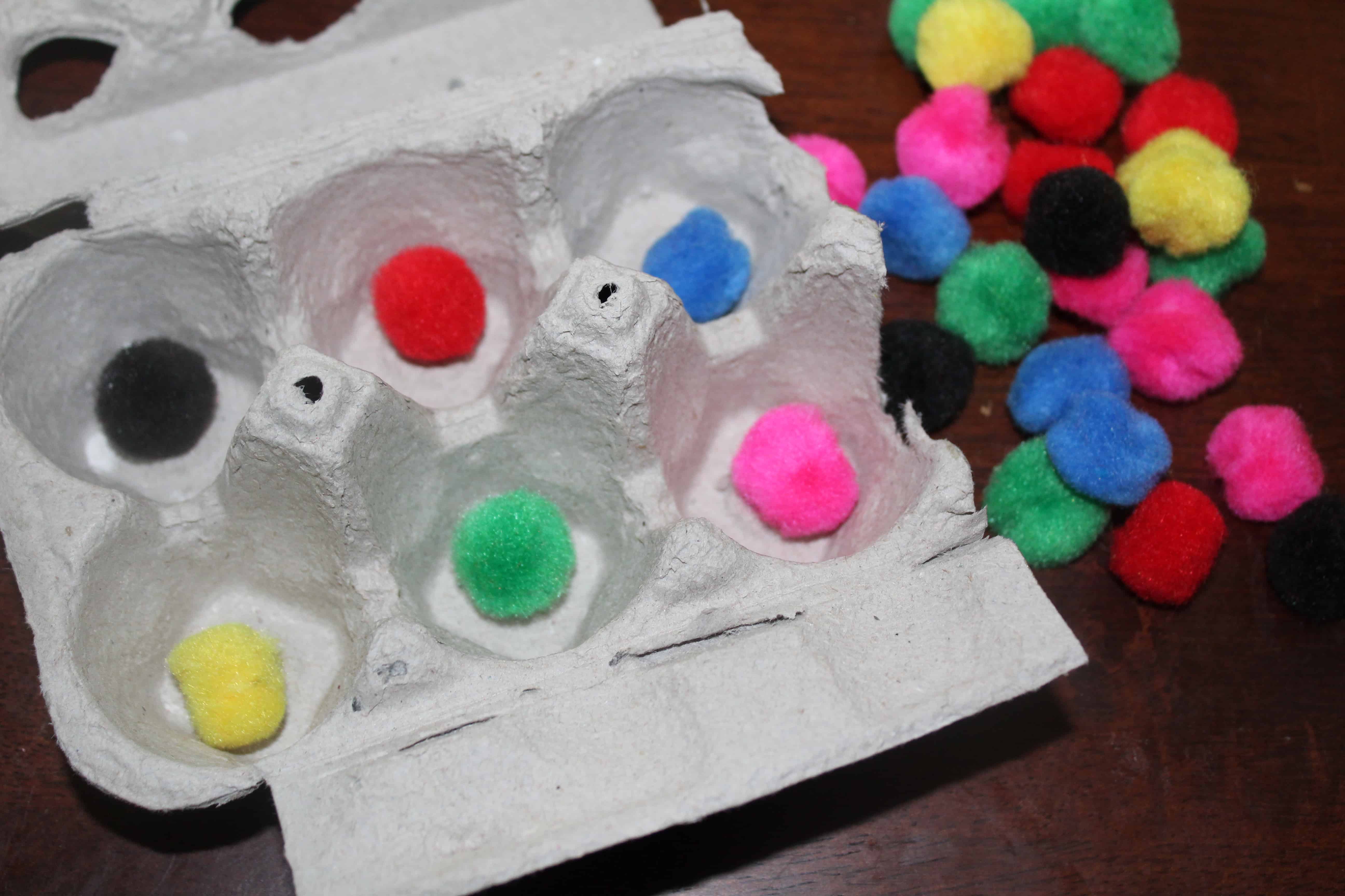 Egg carton half with sorted color cotton pom poms 