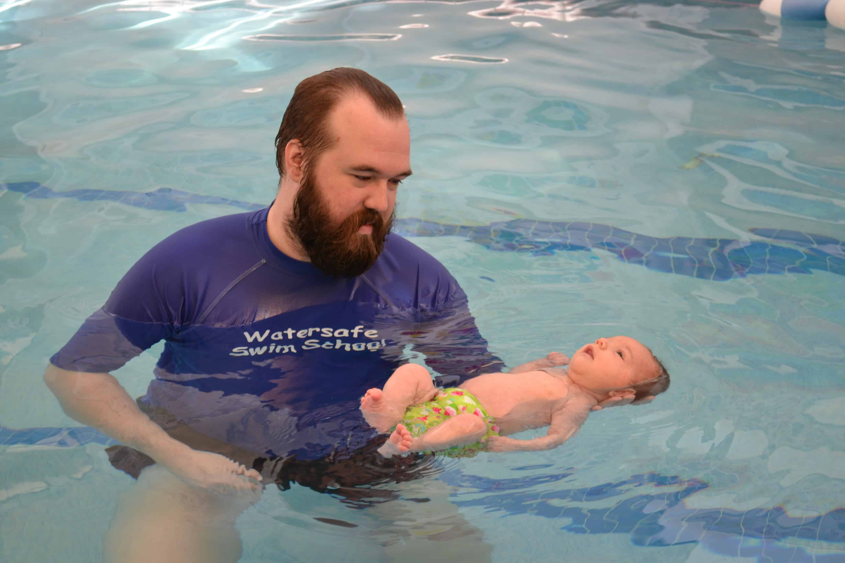 Swim instructor holding and infant in the water the baby is floating on it's back. 