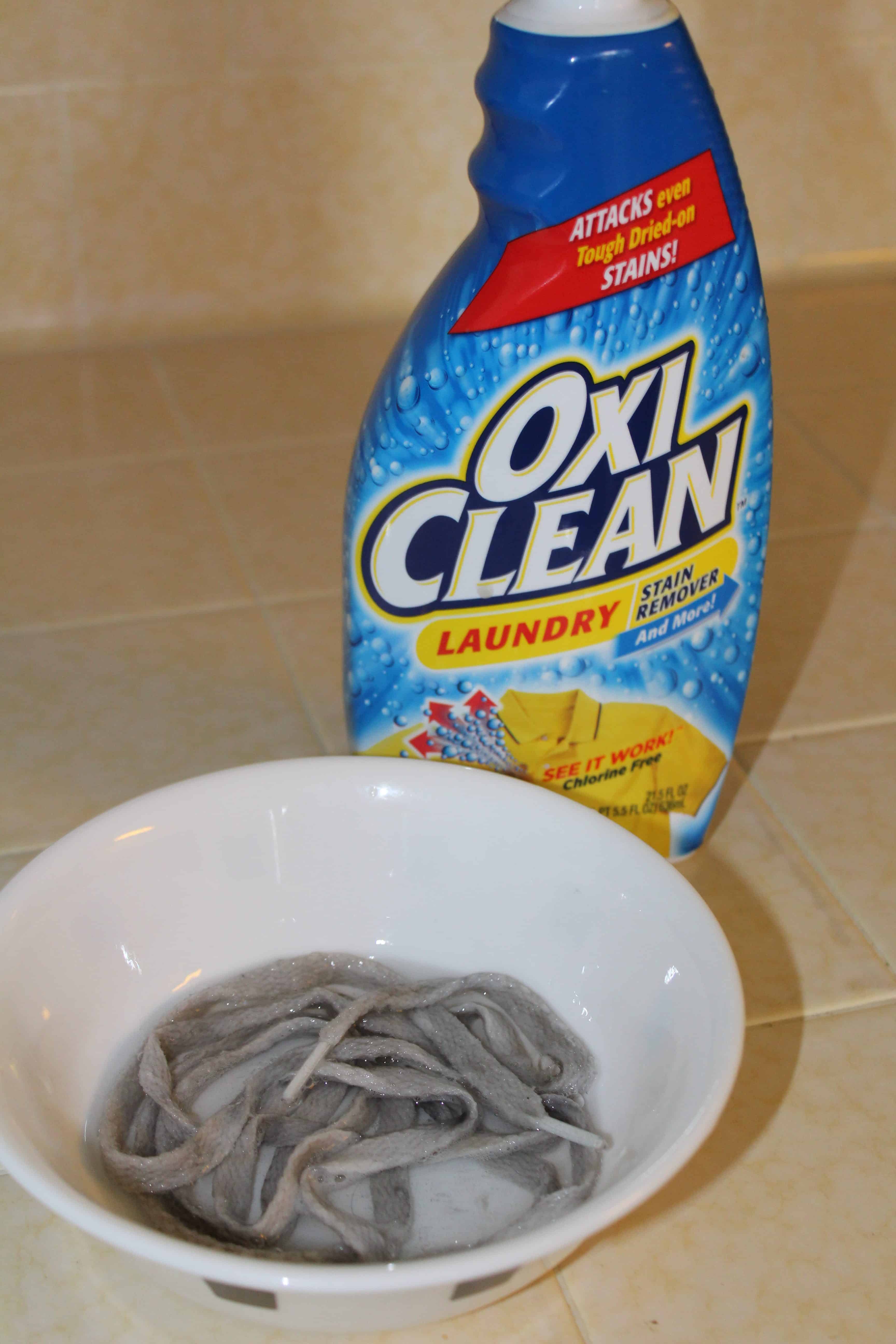 A bowl with dirt shoe laces soaking in solution with an oxi clean bottle in the back. 