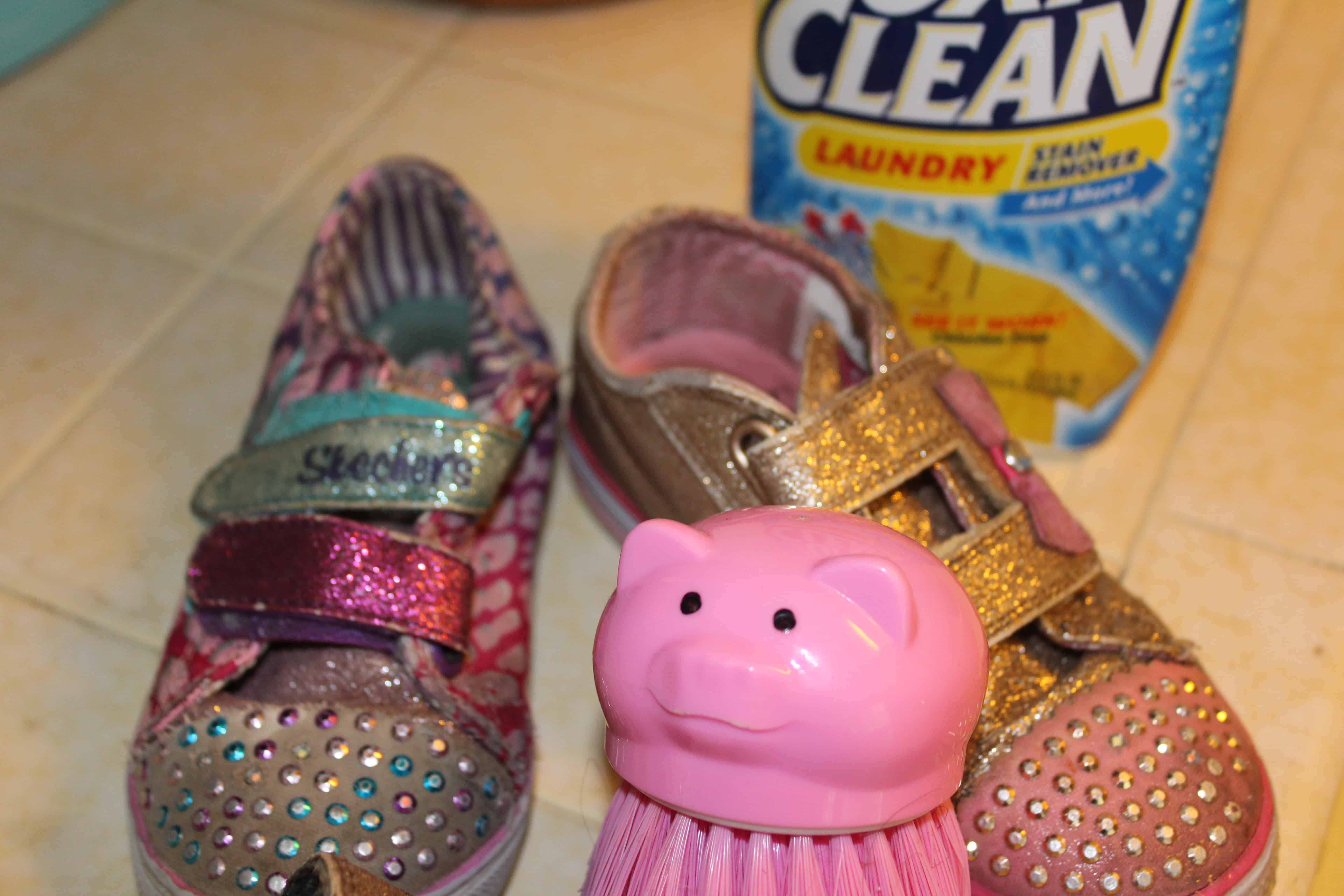 A pair of dirty shoes sitting next to a pig shaped scrub brush with a bottle of Oxiclean in the back ground