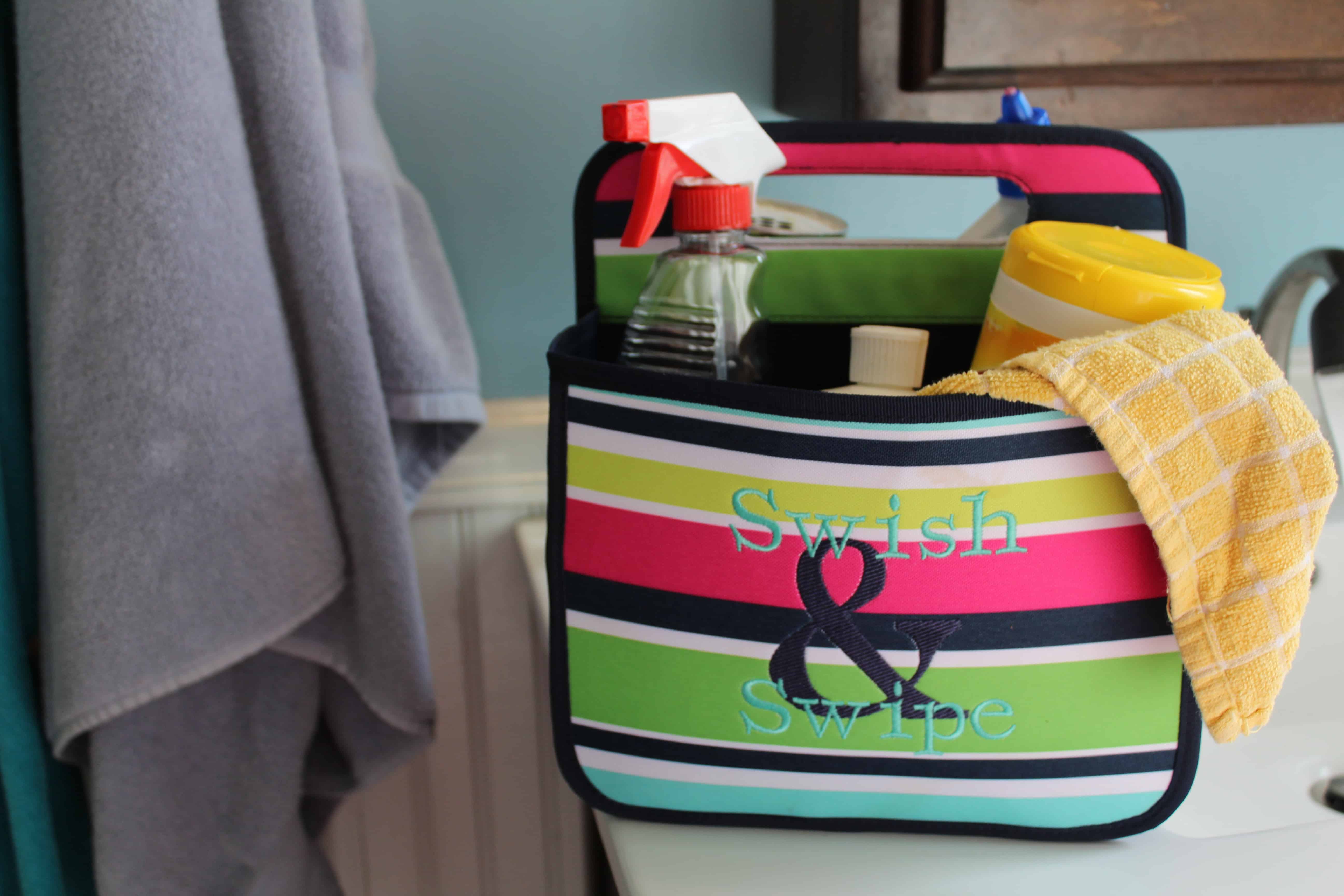 31 Bathroom caddy bag with various chemical cleaners and cleaning rag inside of it. "Swish & swipe" is embroidered on it.