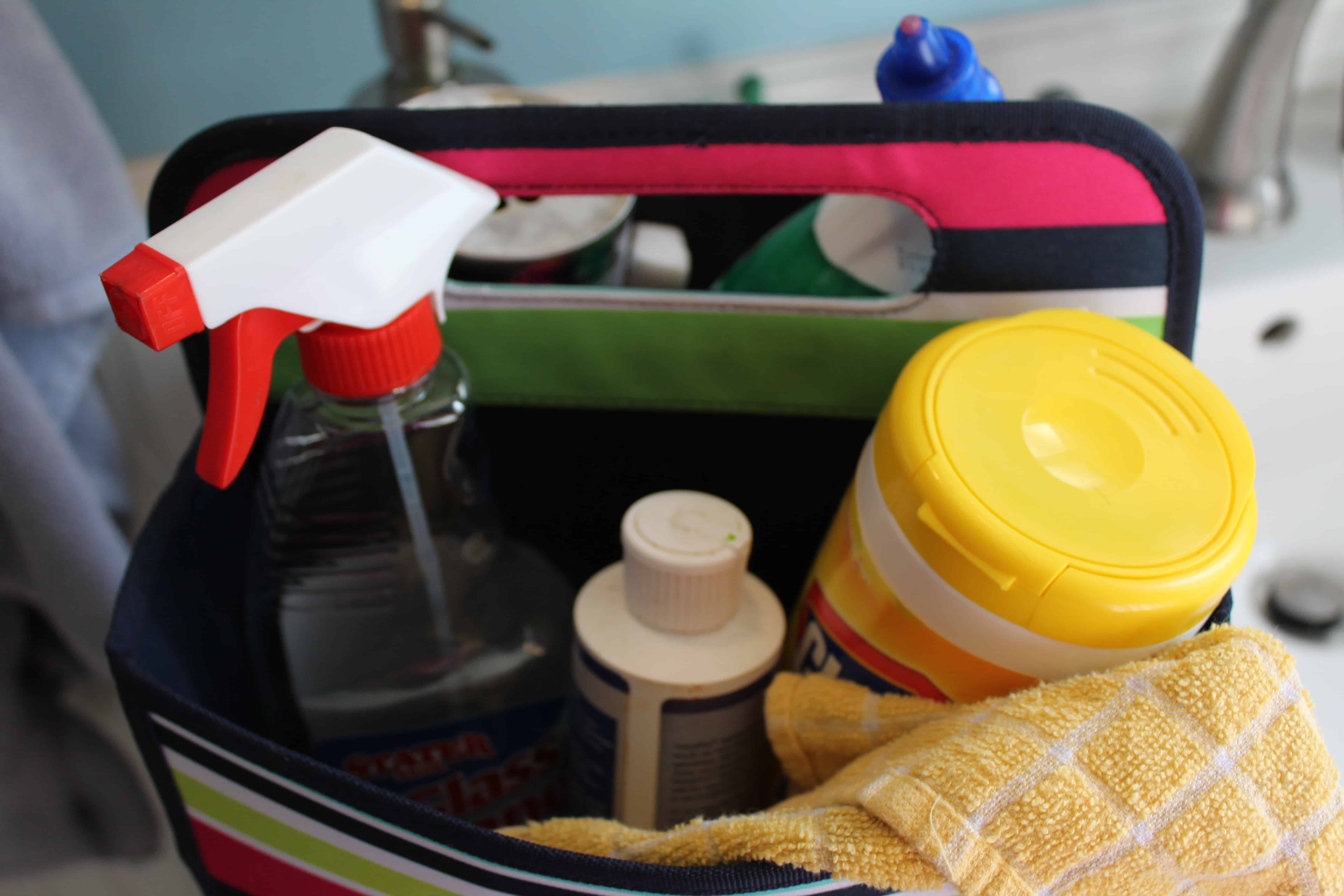 A picture of inside the bathroom caddy bag. A bottle of glass cleaner and a container of clorox wipes are inside with other cleaners and a yellow cleaning rag.