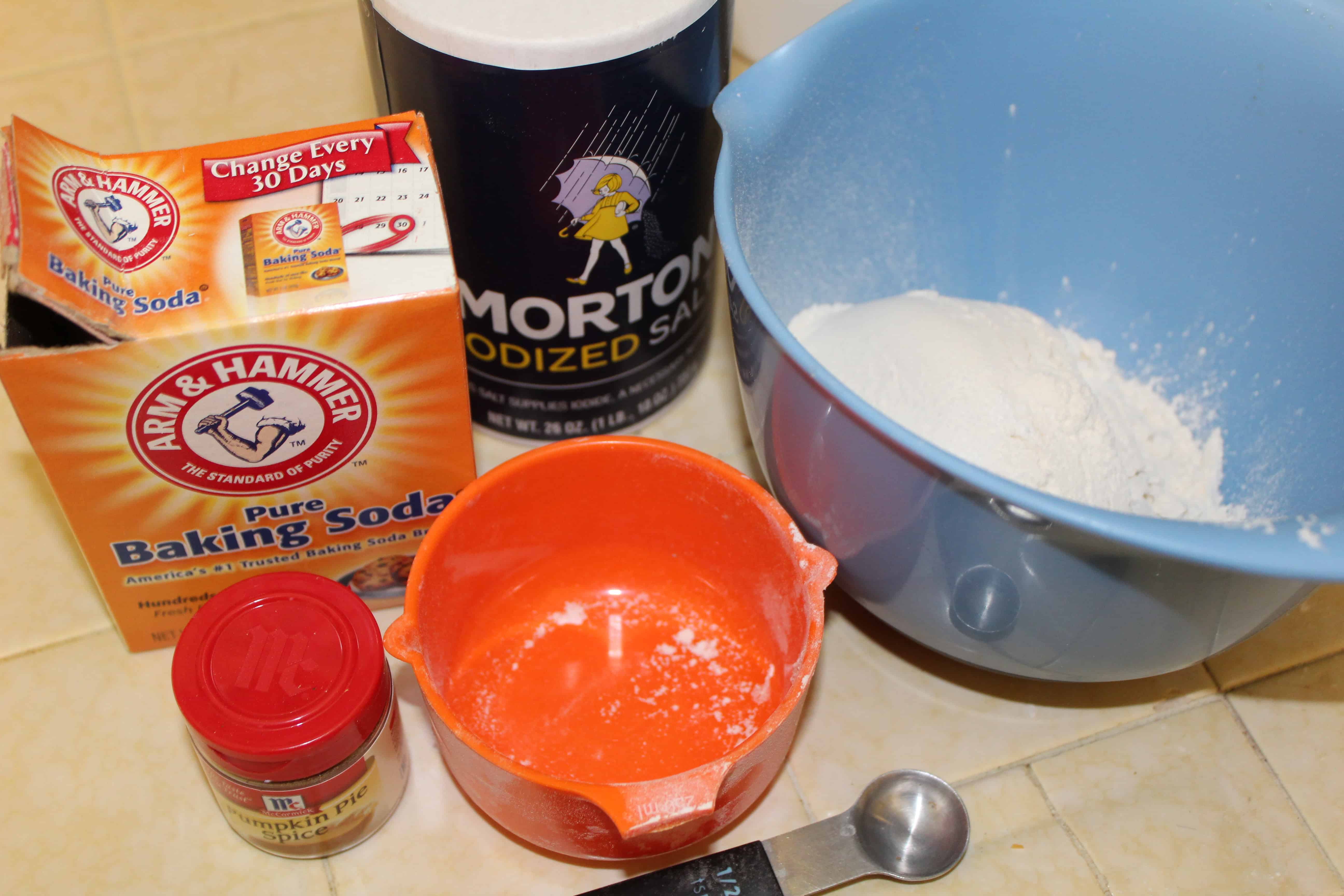 Dry ingredients next to a bowl. Containers of Salt, baking soda and pumpkin spice sitting on the counter. 