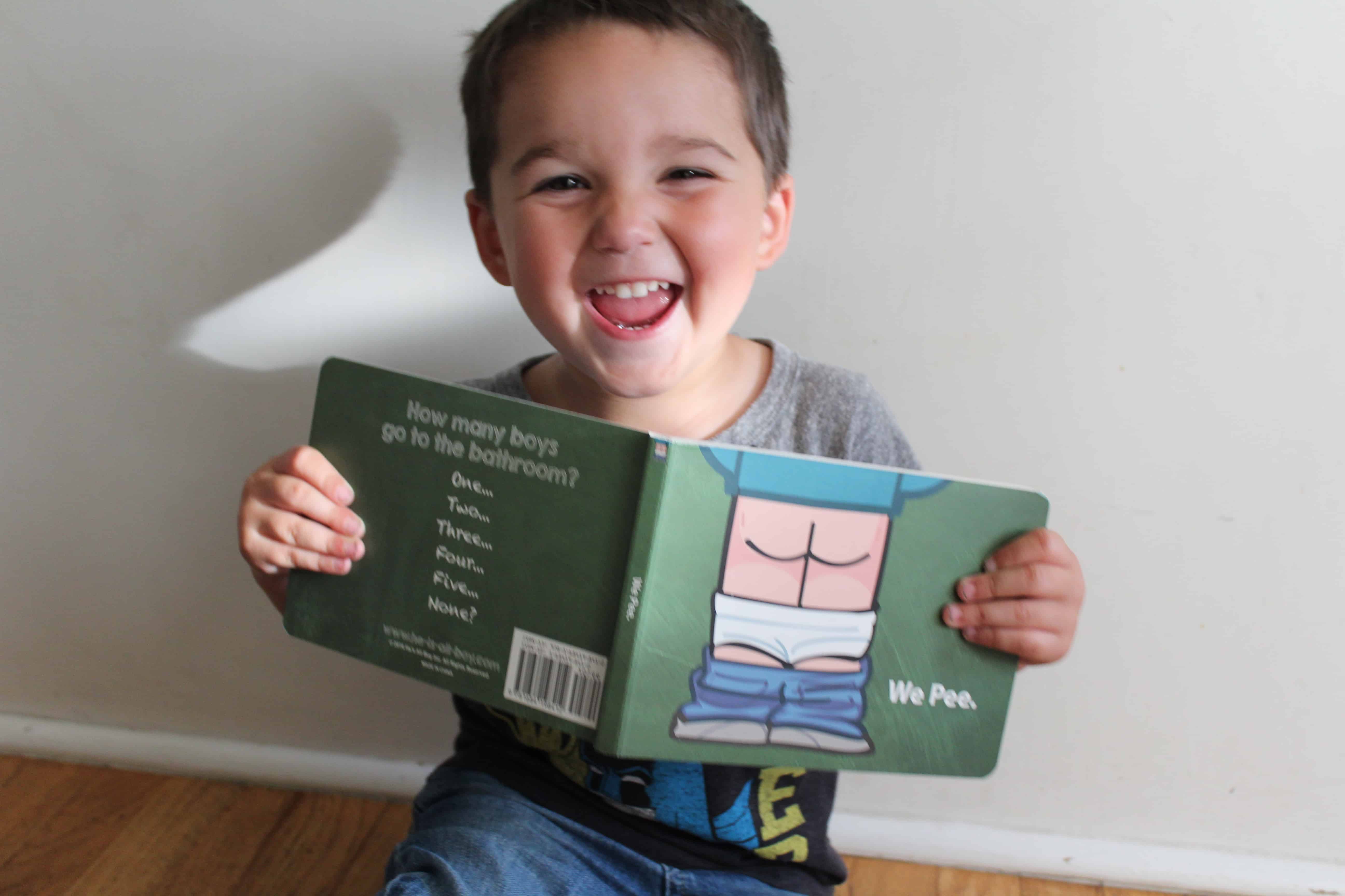 Smiling toddler boy holding the book called "We pee" 