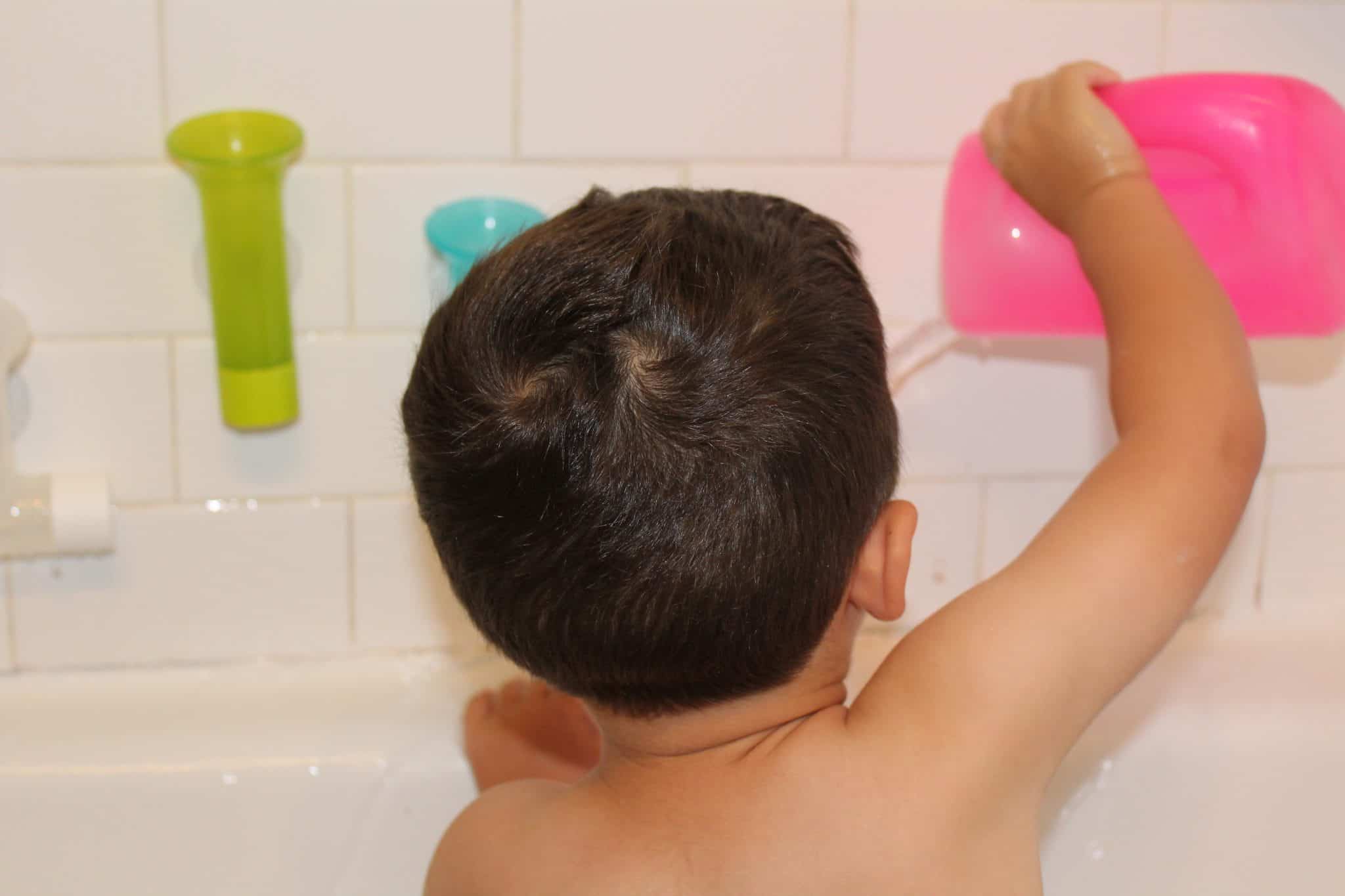Toddler in the bath tub playing with toys