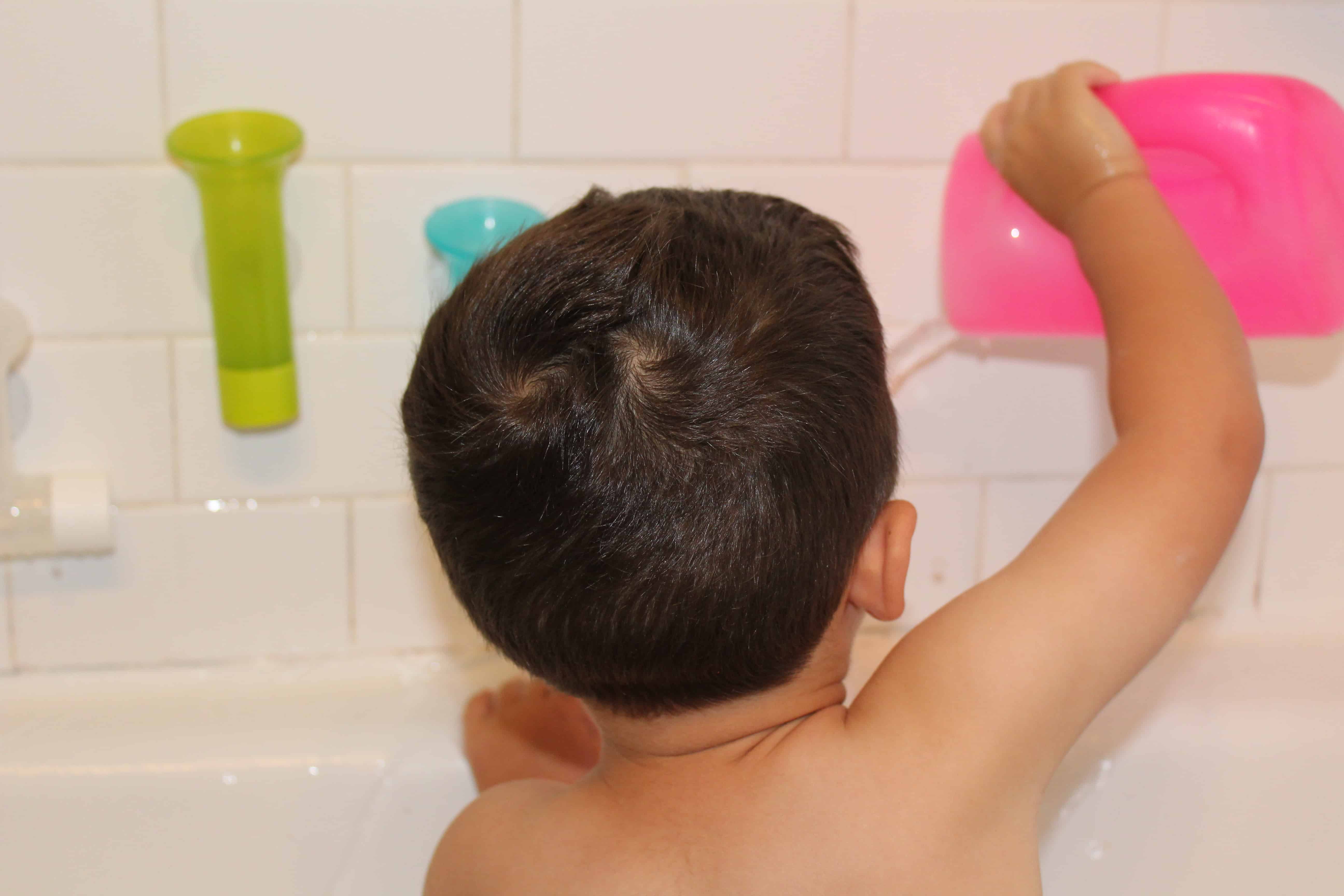 Toddler facing away from camera pouring water into bathtub.