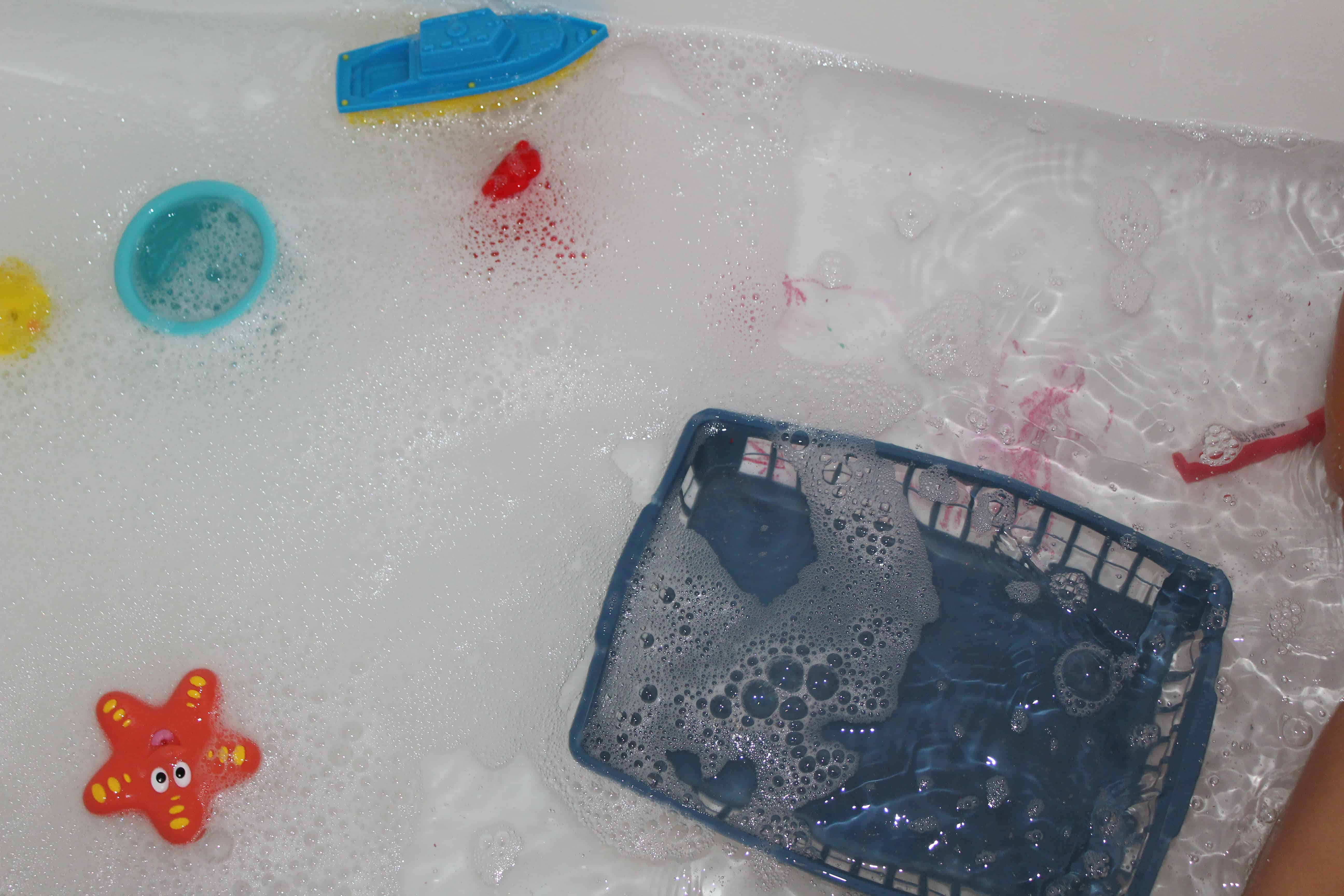 floating plastic and rubber toys floating in soapy water and a plastic basket. 