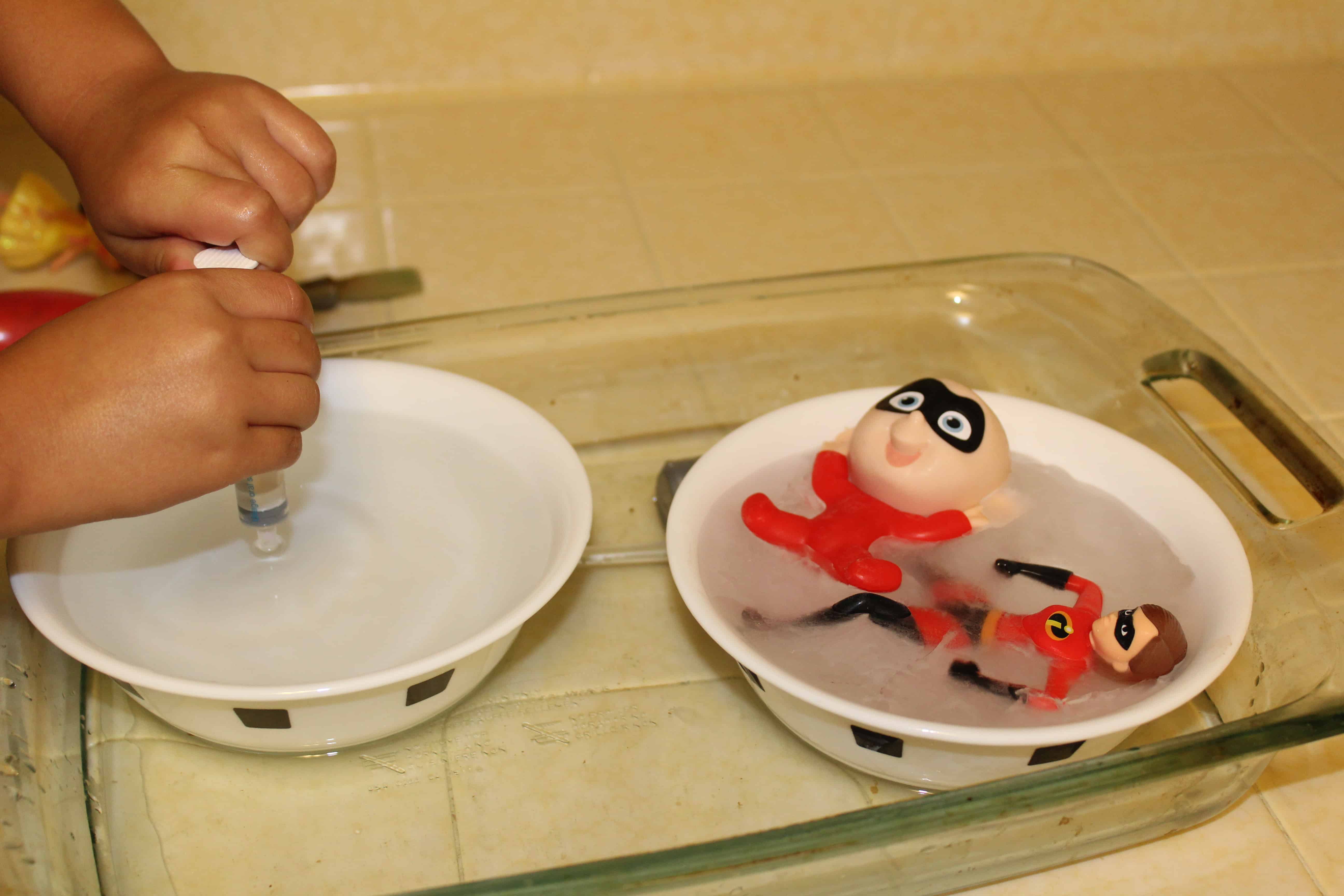 Child practicing with syringe to gather warm water from one bowl to put in the other bowl.