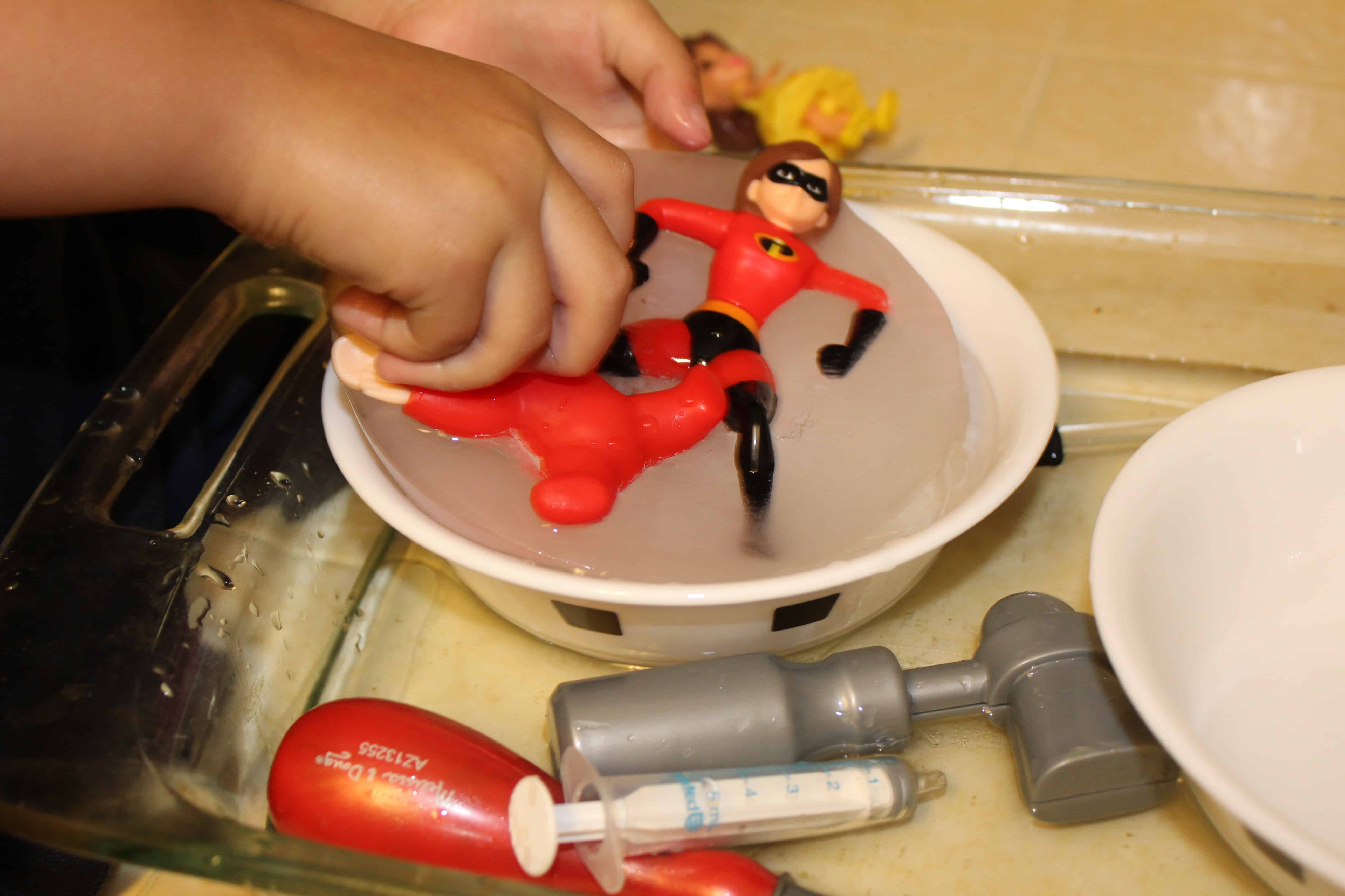 Toddler hands working to free action figures from ice.