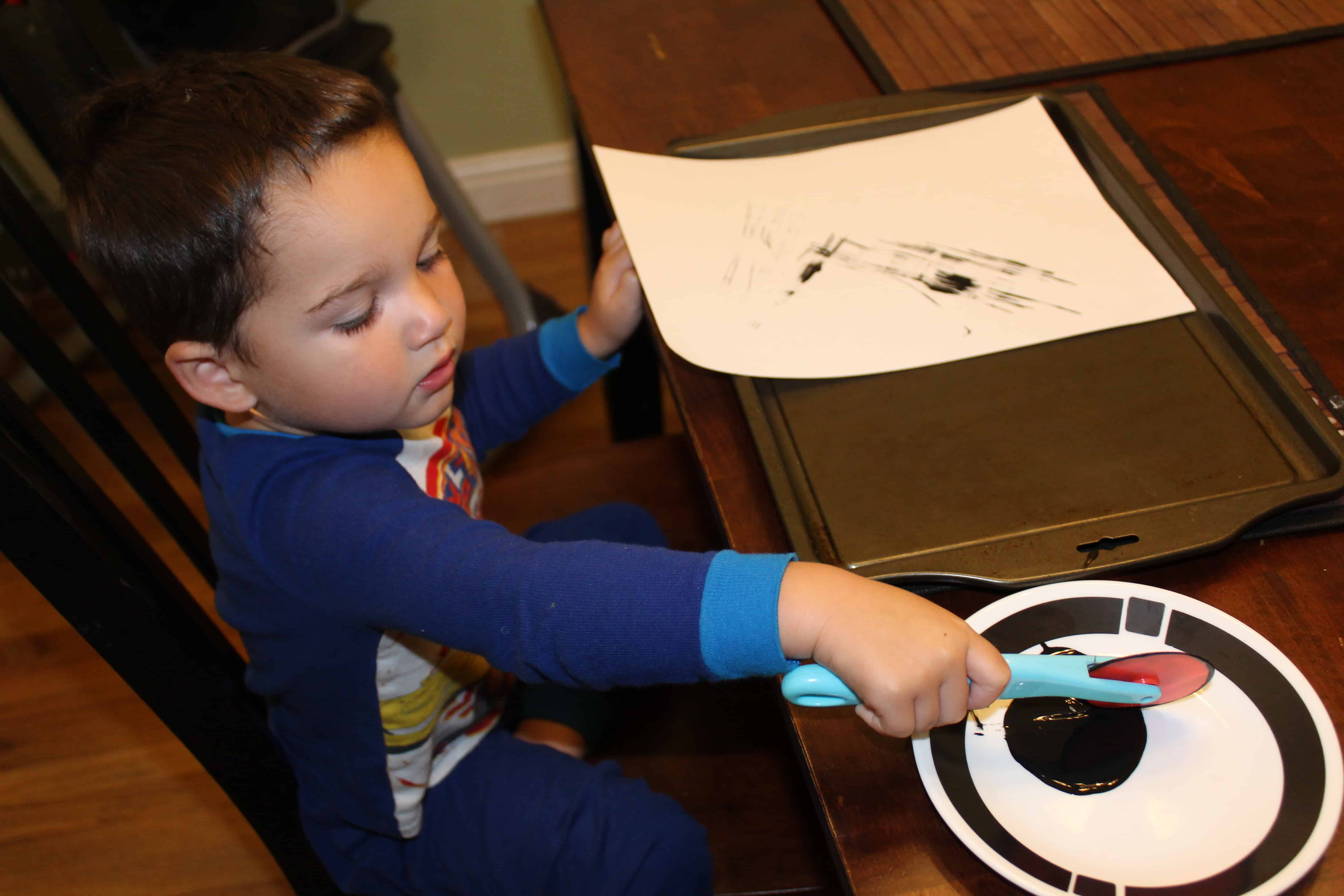 A bit of black paint on a plate toddler using playdough tool to paint