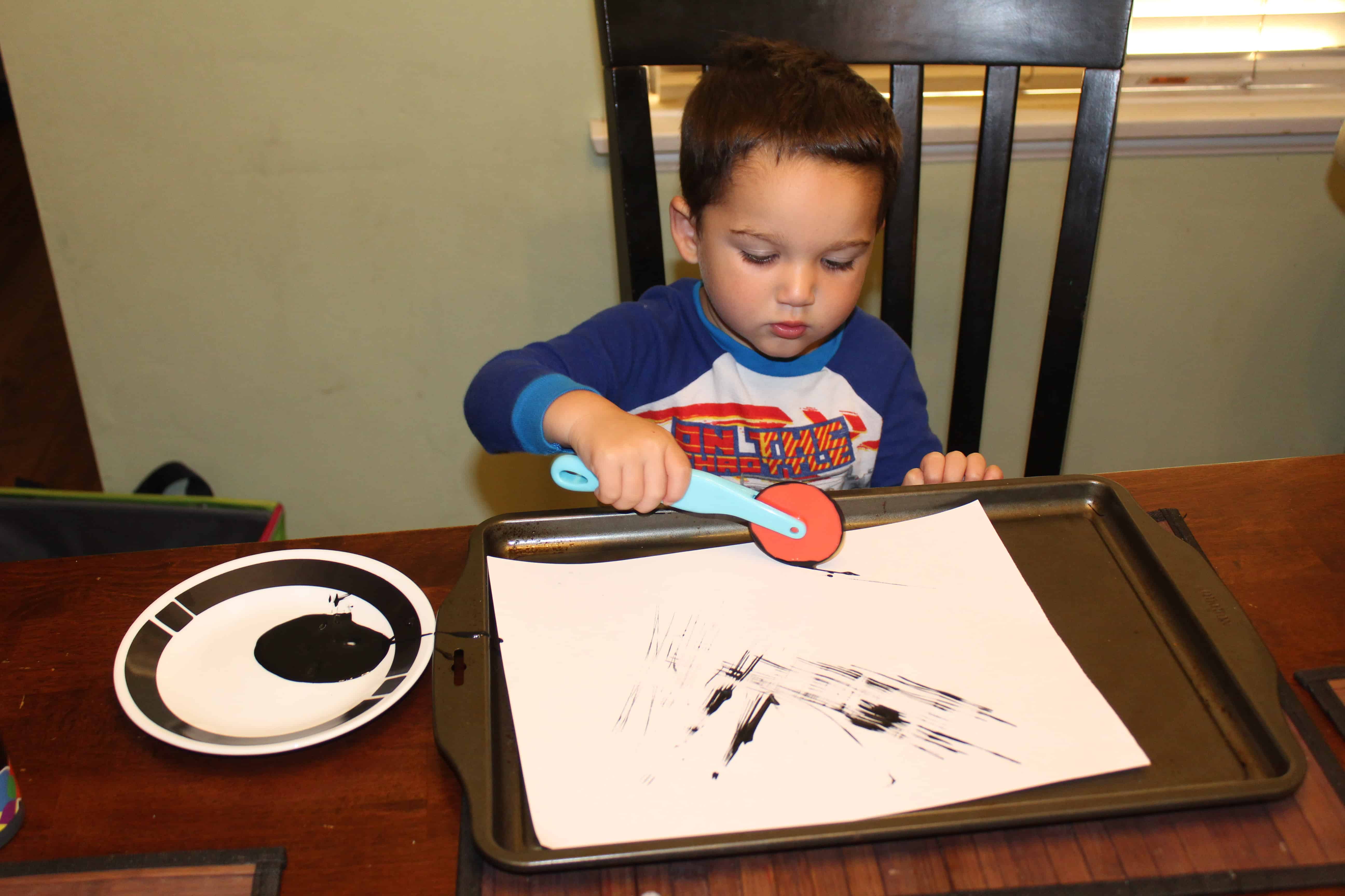 Toddler using play dough tool to paint lines on the white sheet of paper. 