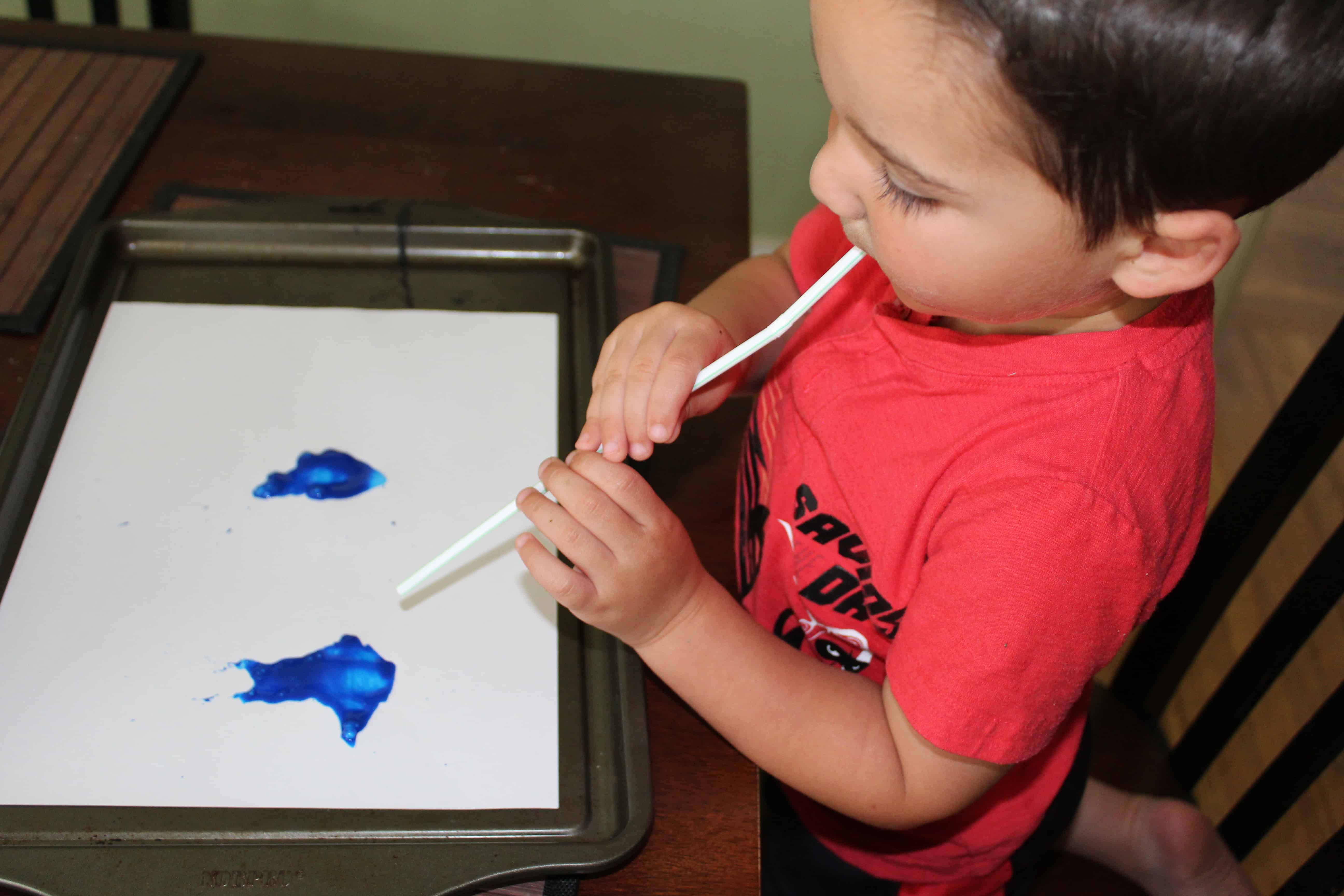 Toddler blowing pain patterns on a white sheet of paper.