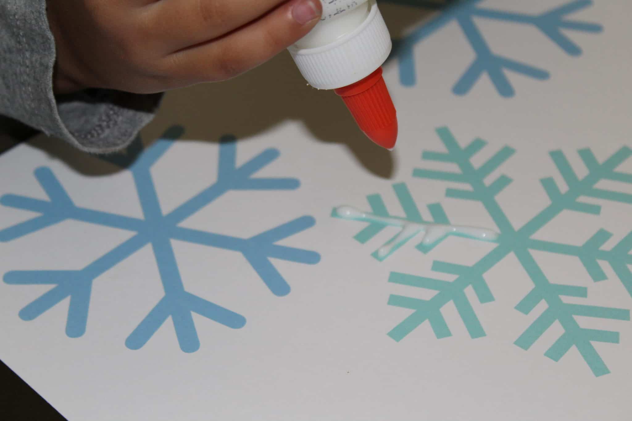 Toddler tracing snowflake with glue bottle.