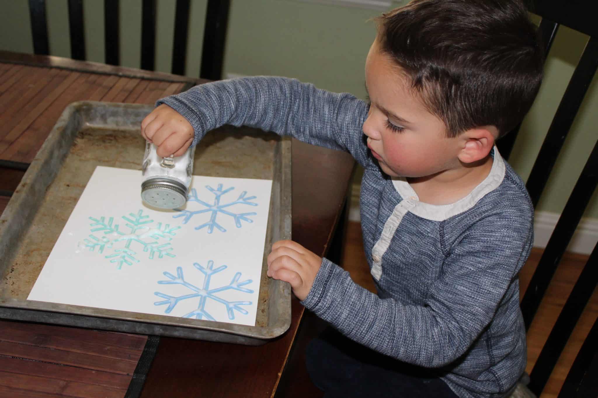 Toddler using salt shaker to cover the glued snowflake template.