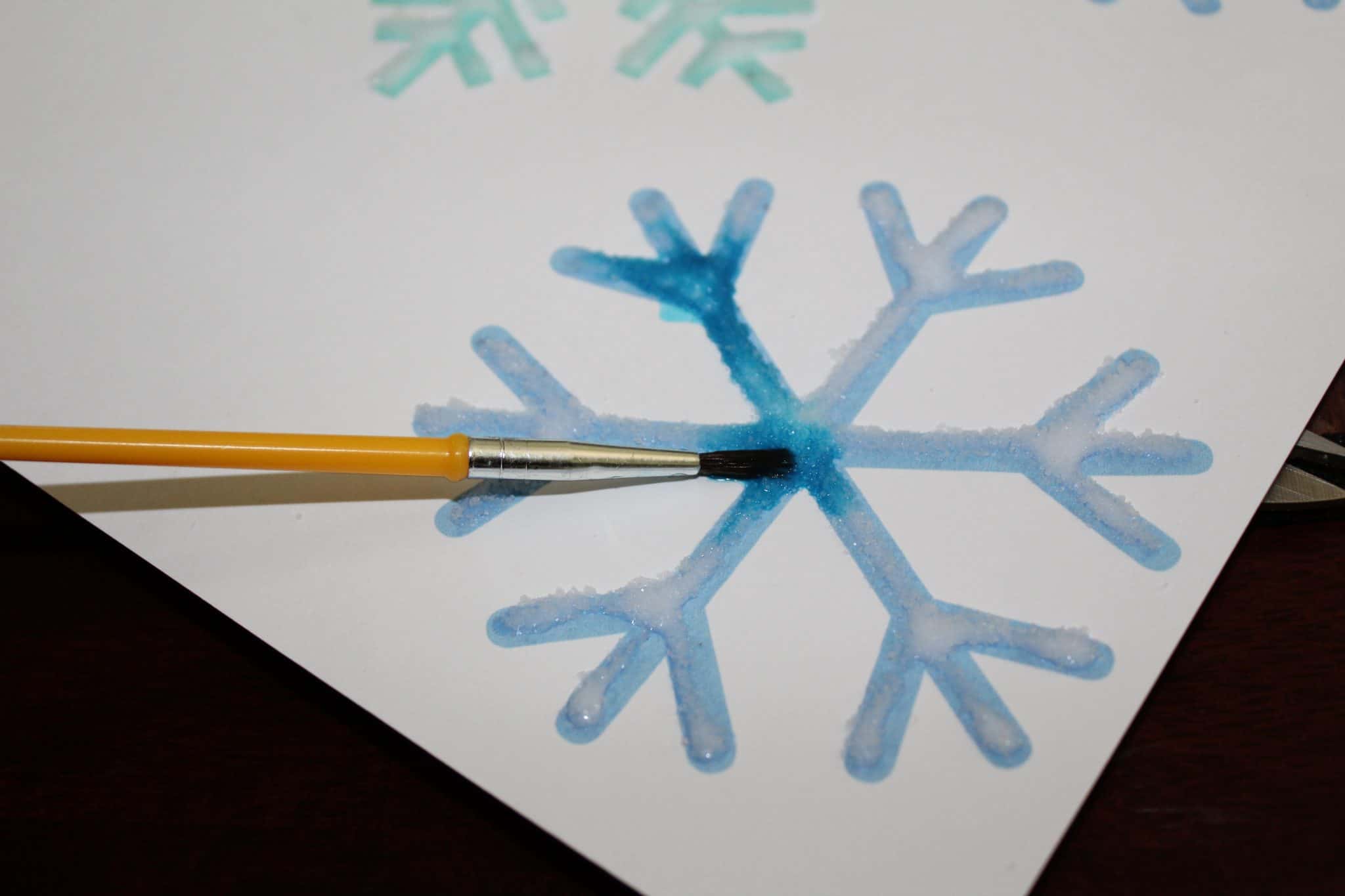 Paint brush with blue watercolor being dabbed onto salted template to paint the salt.