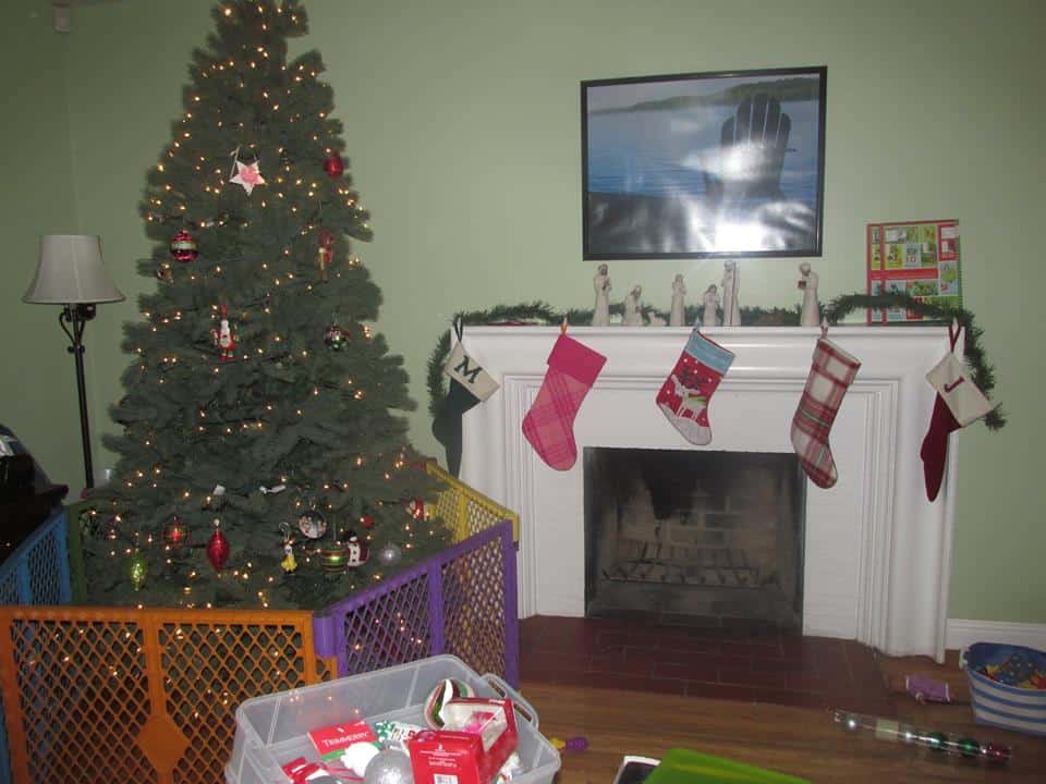 A Christmas tree with a gate around it, along with a Fireplace with stockings hung safely on the mantle. 