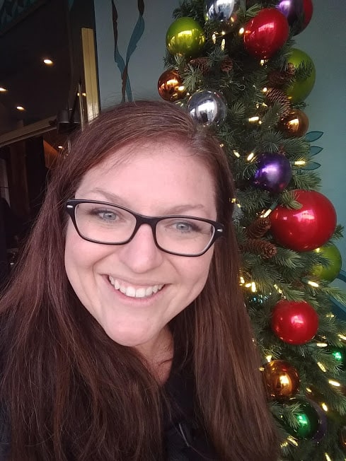 Smiling lady in front of shiny Christmas tree.