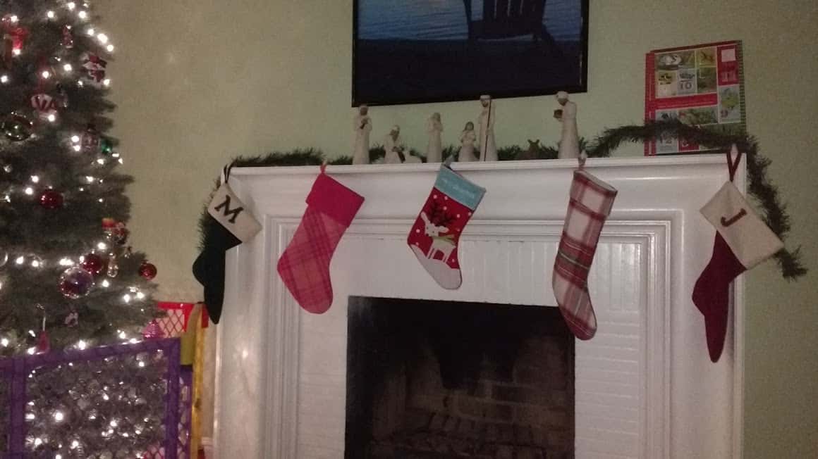 Four Christmas stockings hanging safely from the top of the mantle of the fire place.