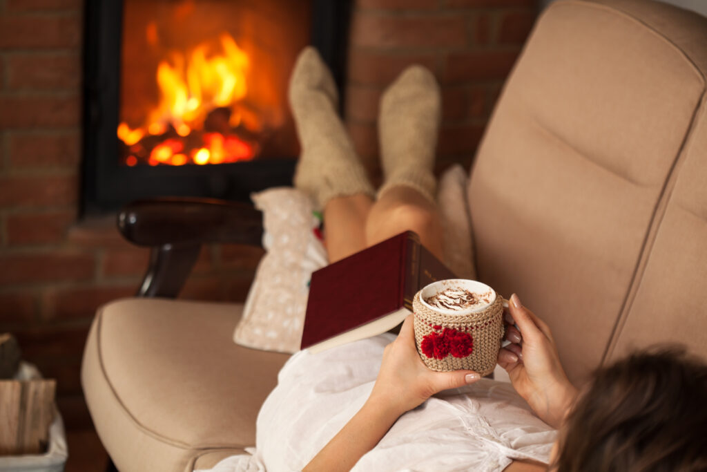 Woman relaxing by the fire holding a cup of hot chocolate with cream on top - lying on a sofa, shallow depth