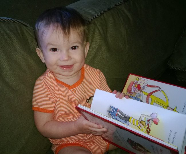 Baby holding a book to look over. 