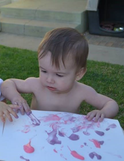 Toddler painting outside with a paintbrush