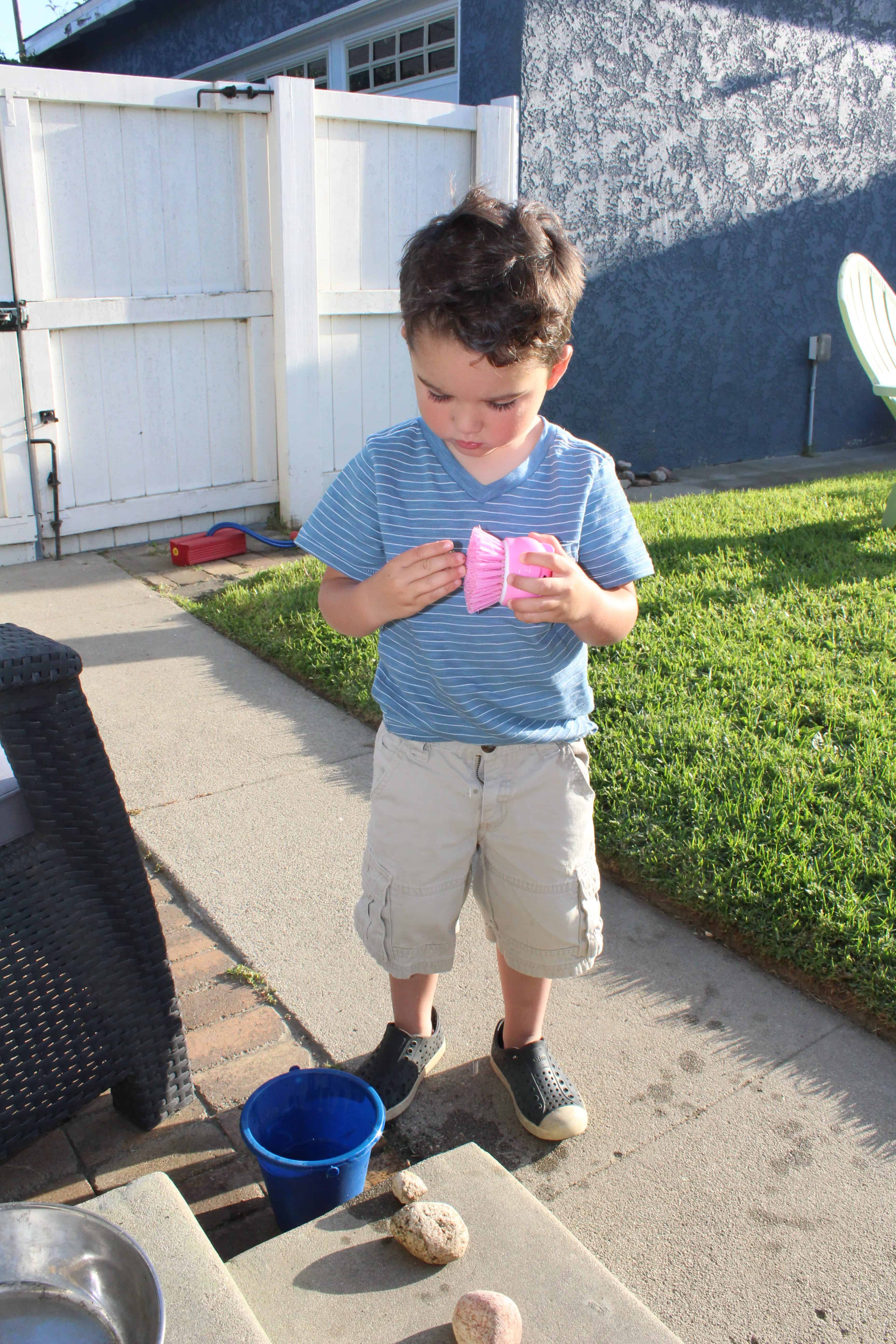 Toddler using a scrub brush to clean a rock