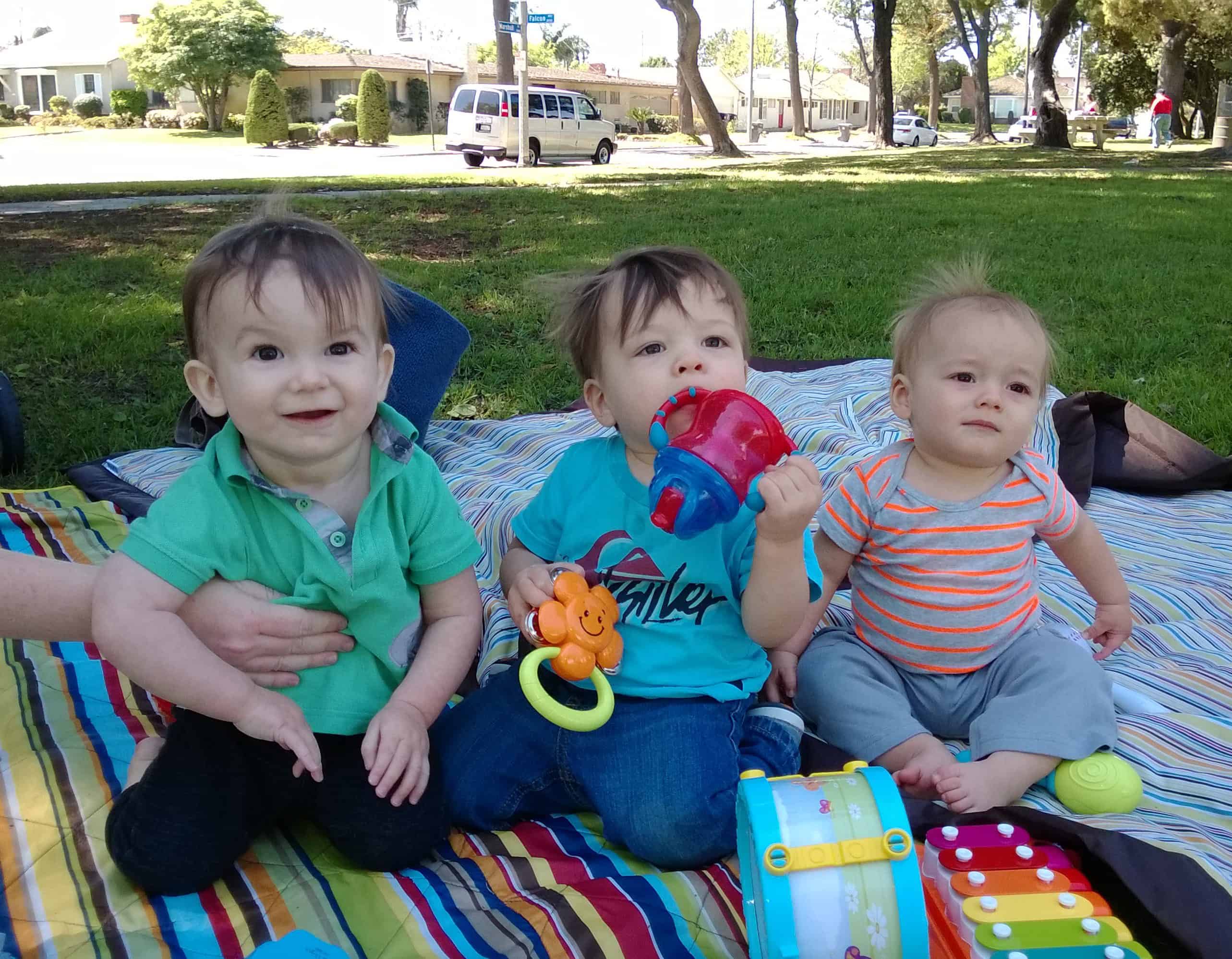 Three young babies sitting on a mat for socialization time.