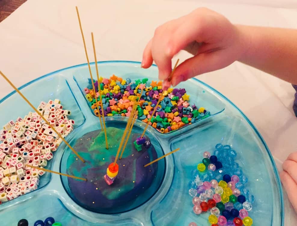 threading beads onto spaghetti in playdough