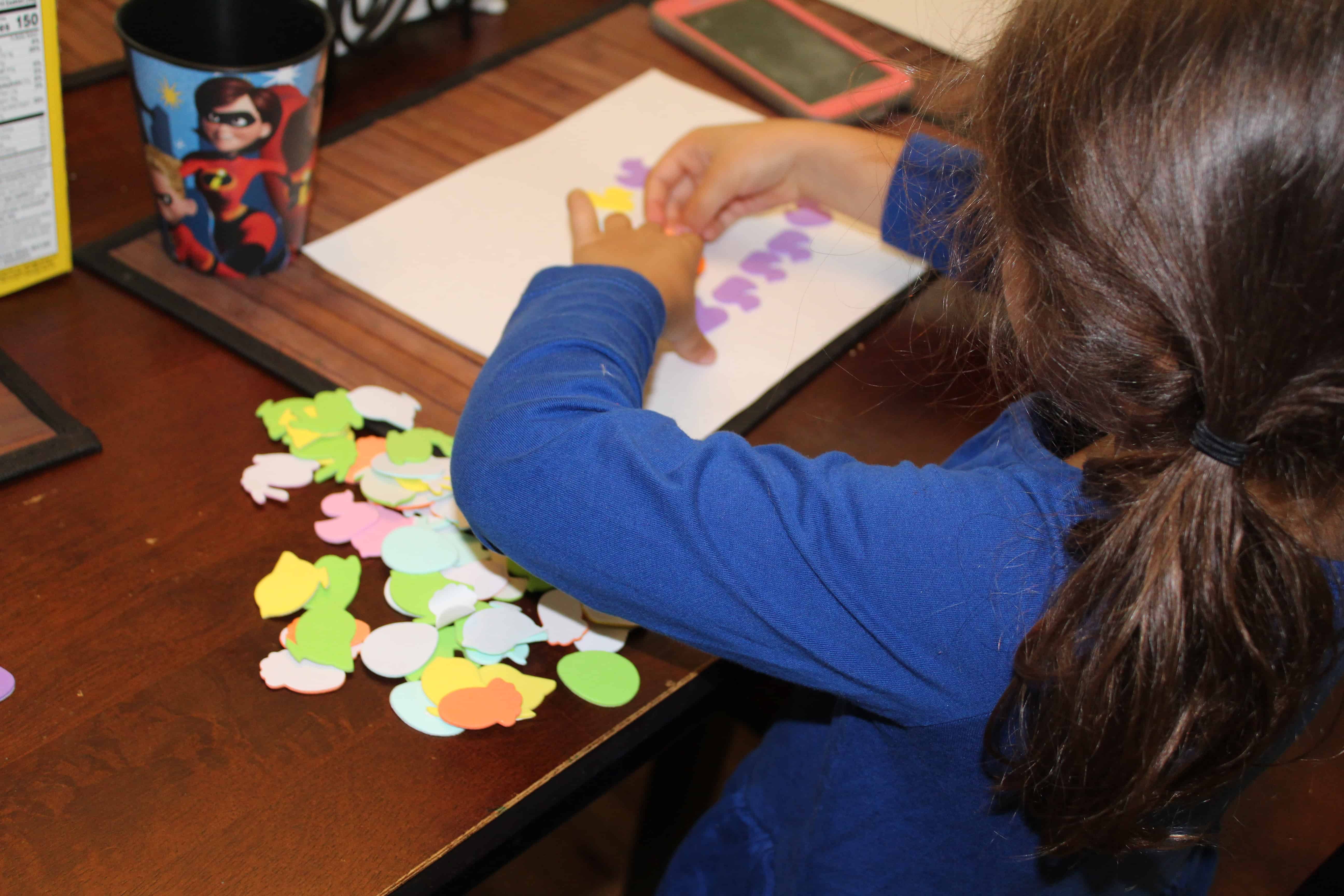 Child using foam stickers on white paper. 