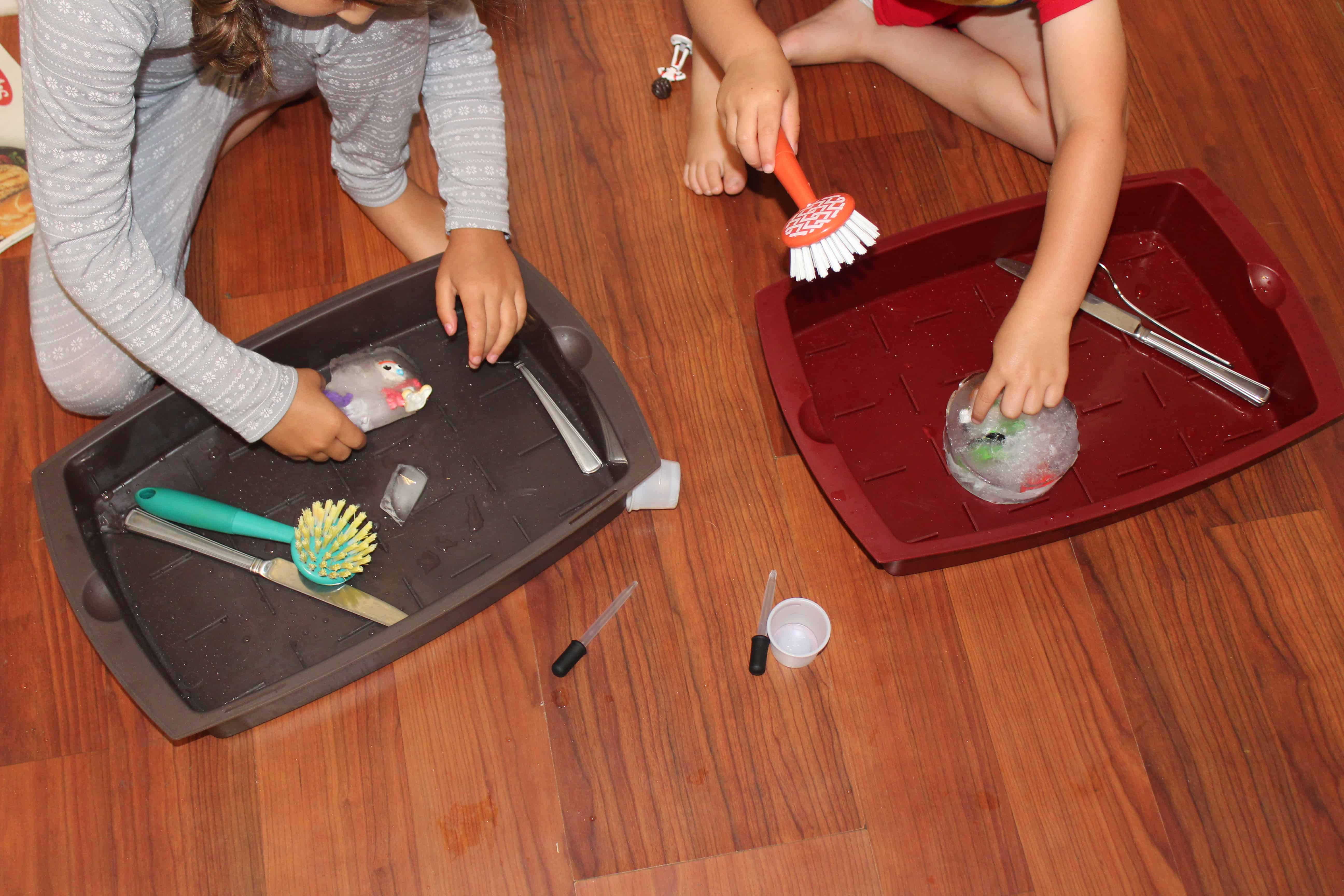 Two children with baking trays rescuing frozen toys from ice