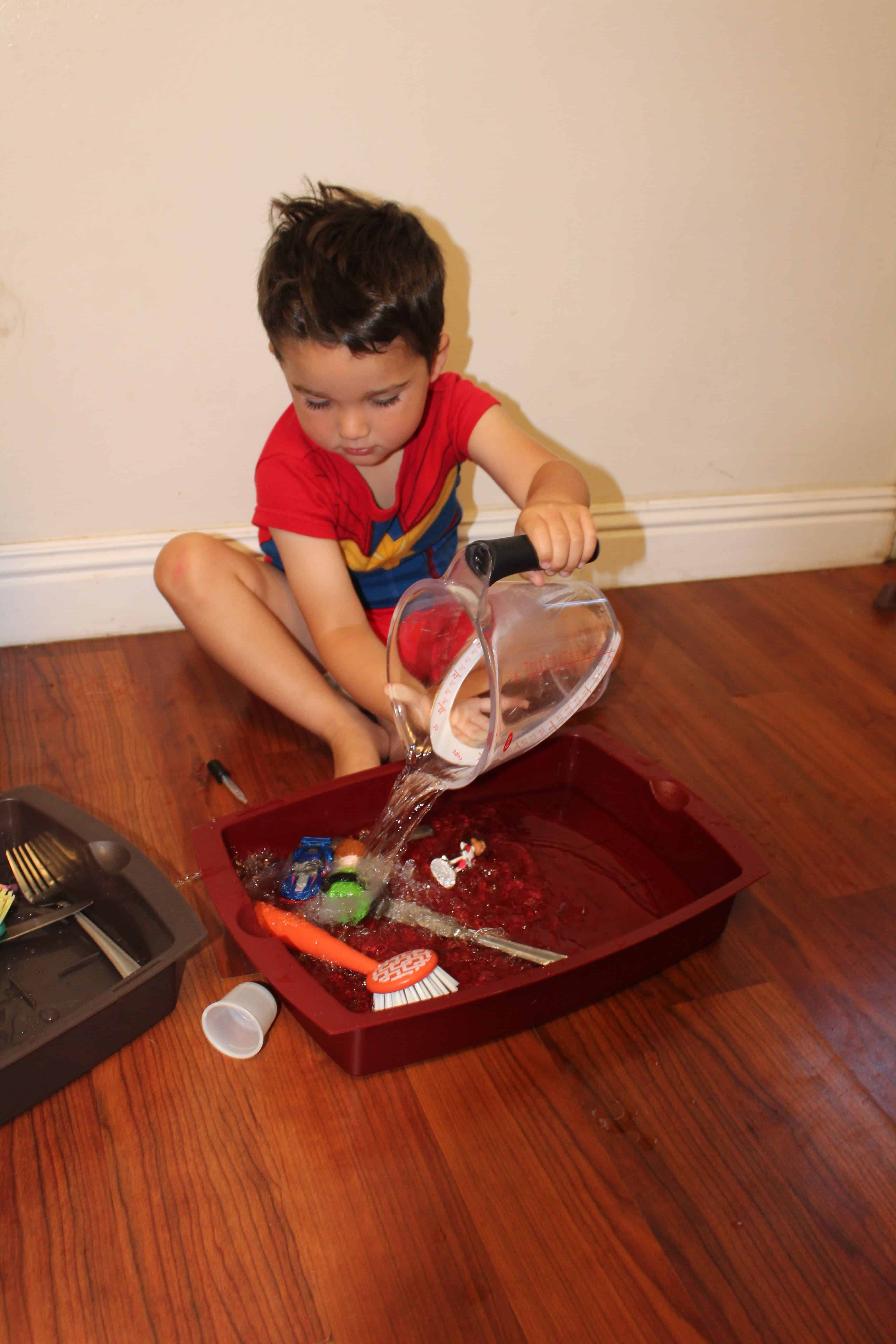 Toddler pouring water from a measuring cup into a baking tray