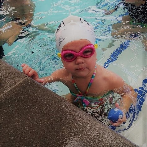 Toddler in the pool sitting in a swim cap with finis on. 