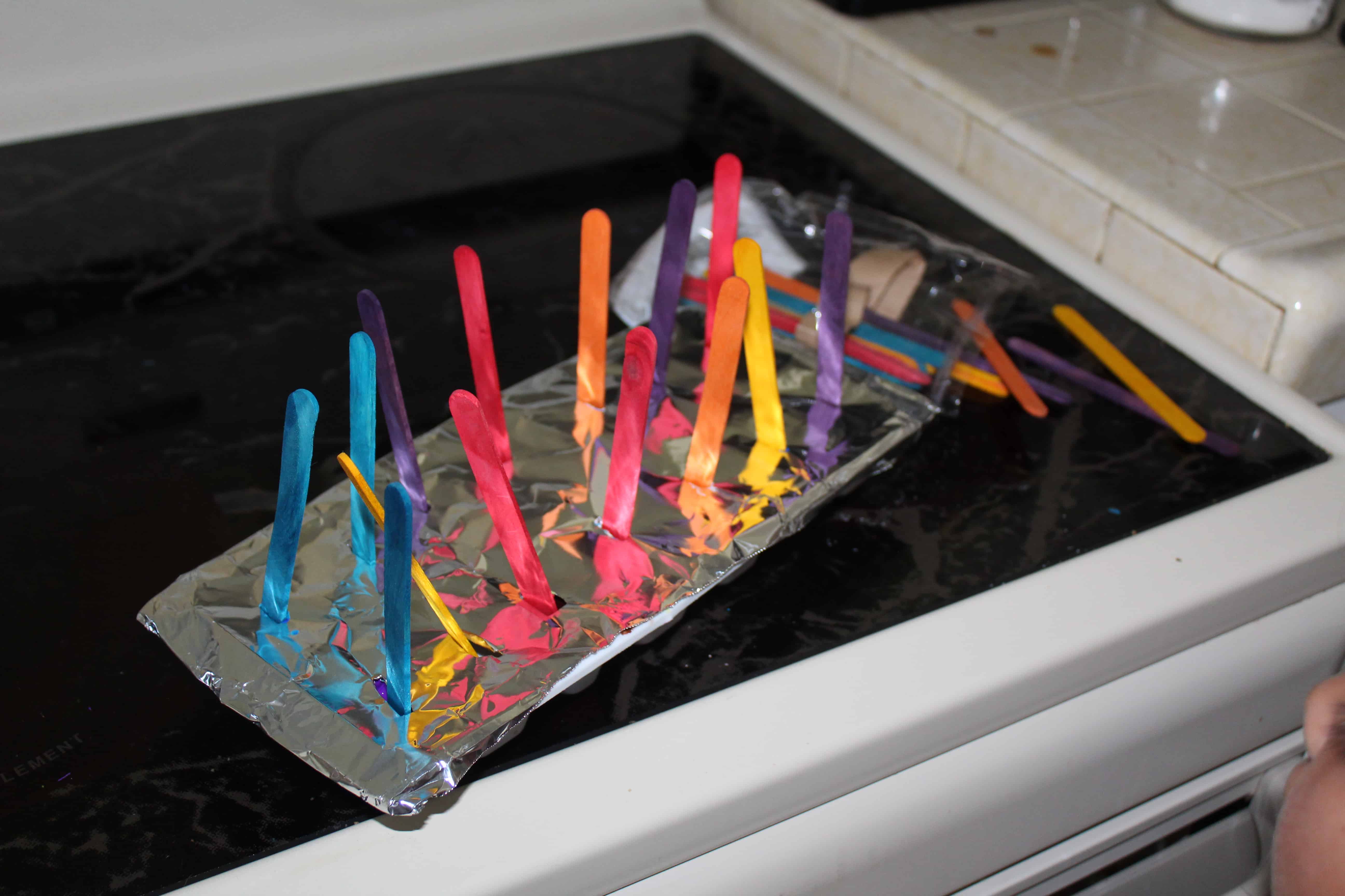Ice tray with foil and popsicle sticks sticking out making DIY ice paint