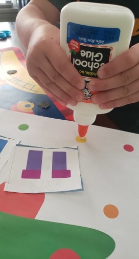 Toddler holding glue bottle placing dot of glue on a Christmas tree activity paper.